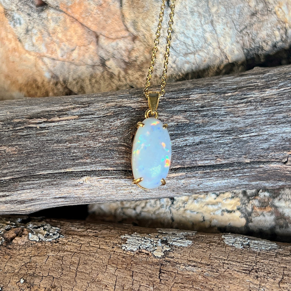 Australian white opal pendant in 18kt yellow gold, blue, red and green pinfire, shown on driftwood
