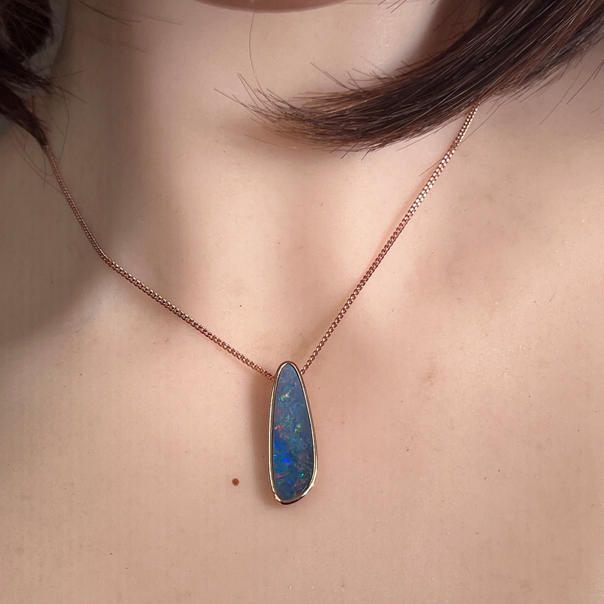 27 x 8mm freeform Australian opal doublet pendant worn at the neck, rose gold-plated silver