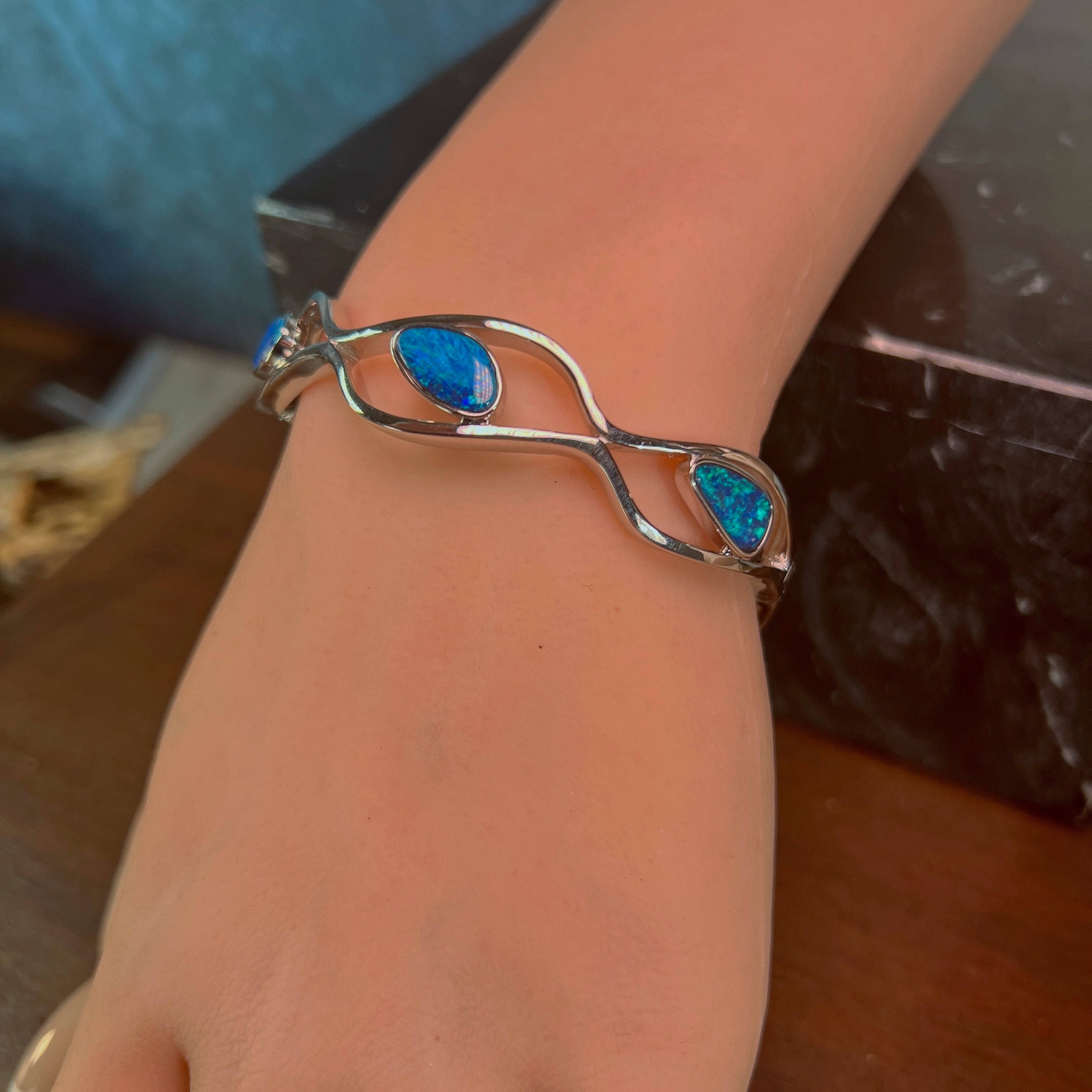 Opal doublet bangle on the wrist, blue-green play-of-colour catching the light