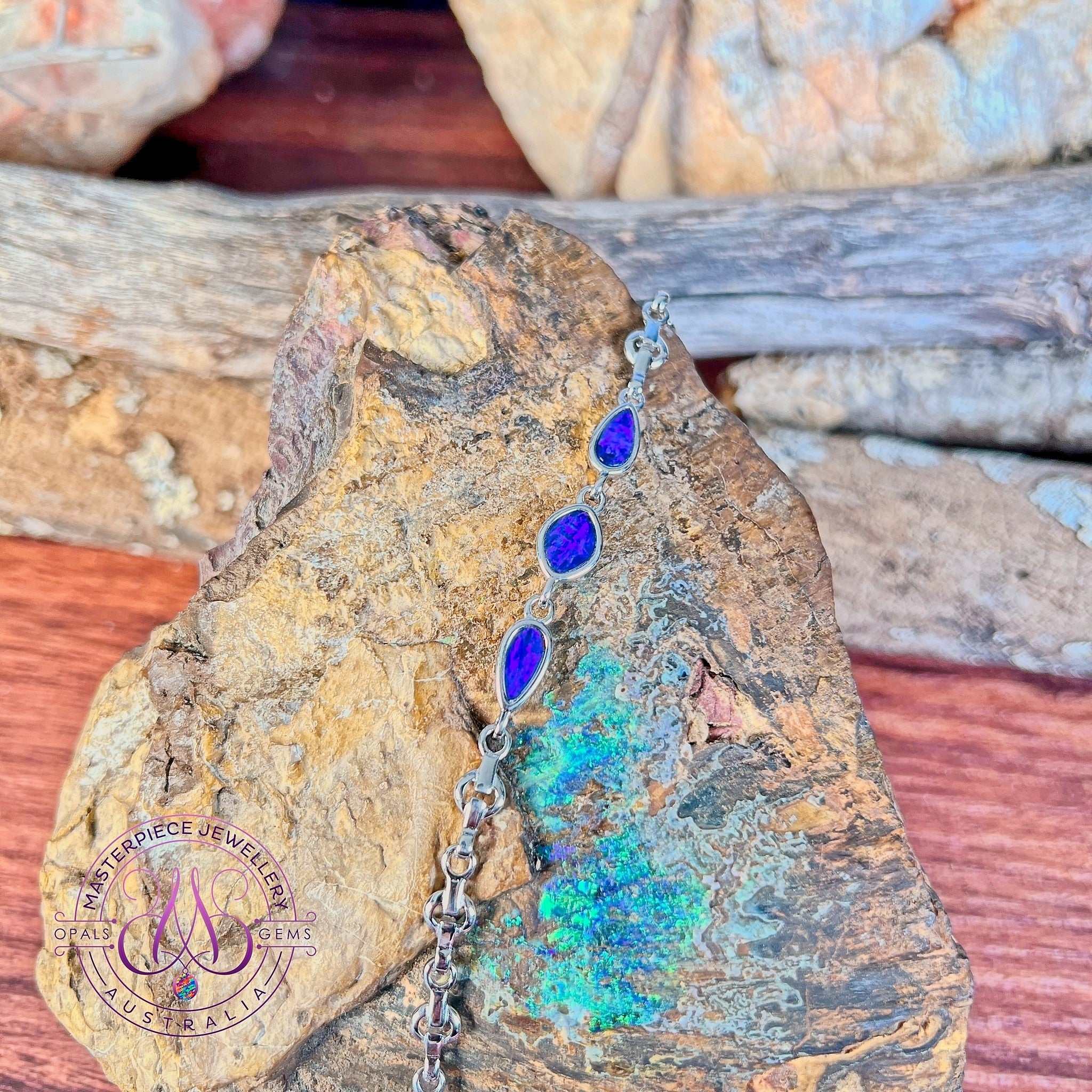 Sterling silver bracelet with three opal doublets resting on rough rock streaked with green and blue