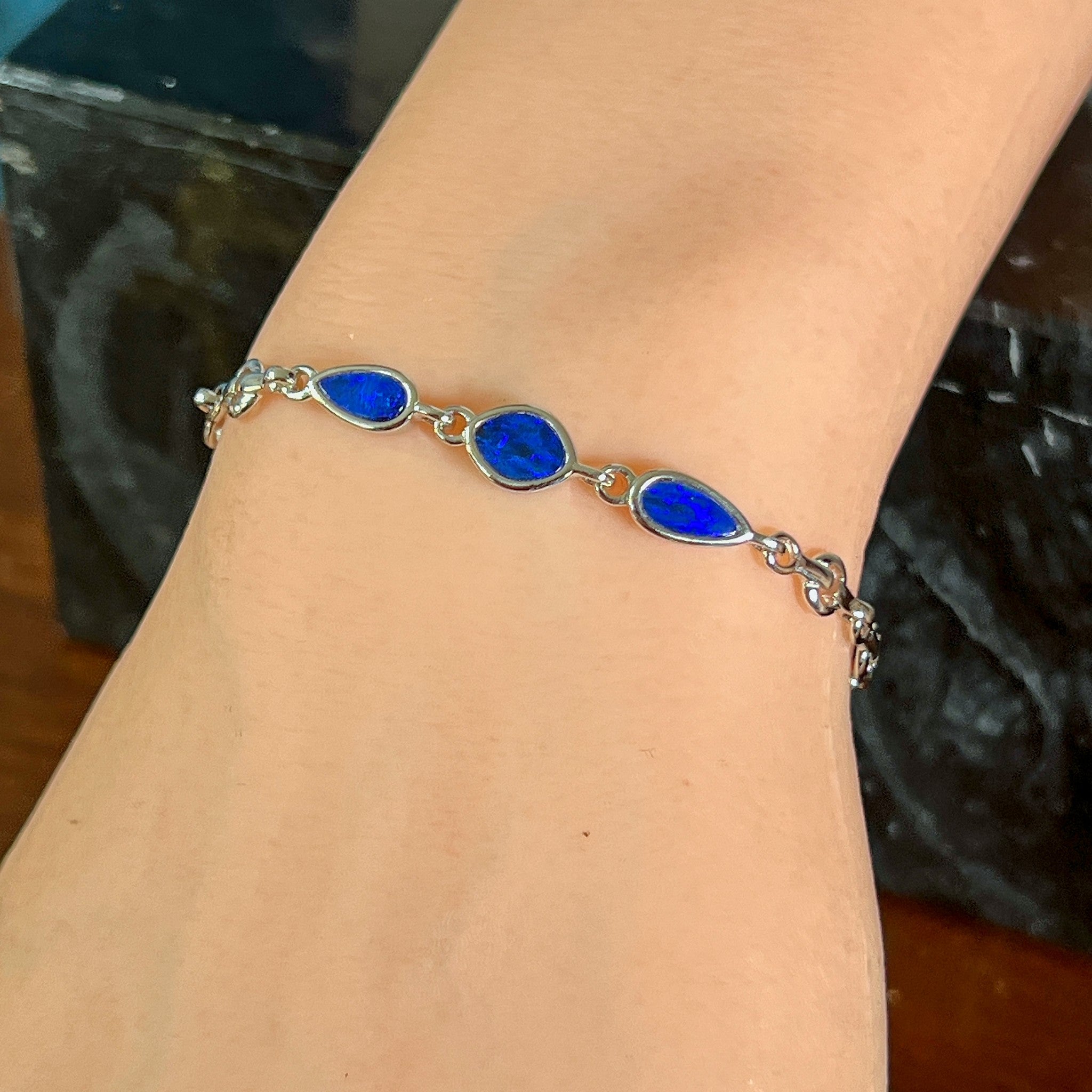 Sterling silver bracelet with three opal doublets on the wrist, angled to catch the blue and black play of colour