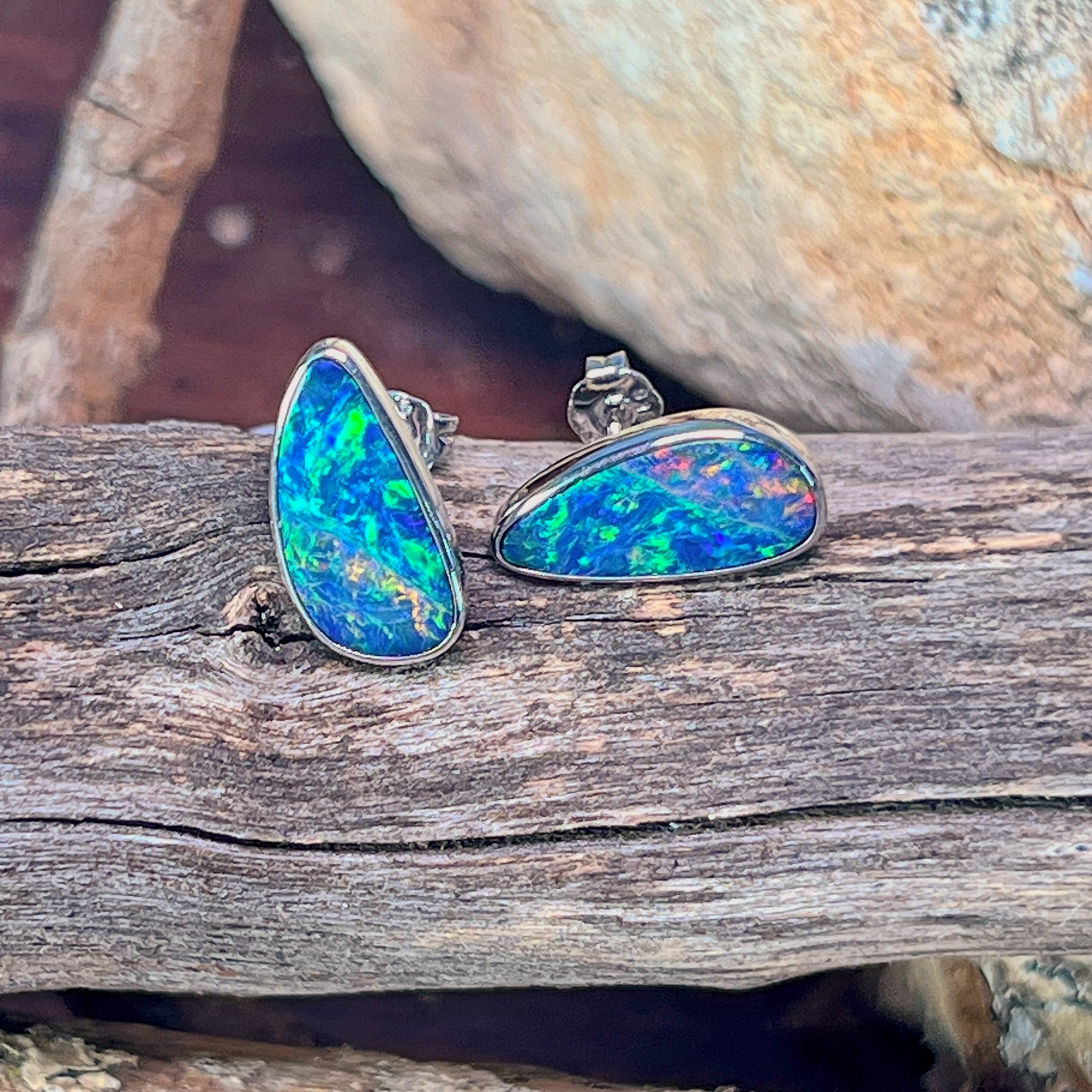 Pair of silver freeform opal doublet stud earrings with butterfly backs on driftwood