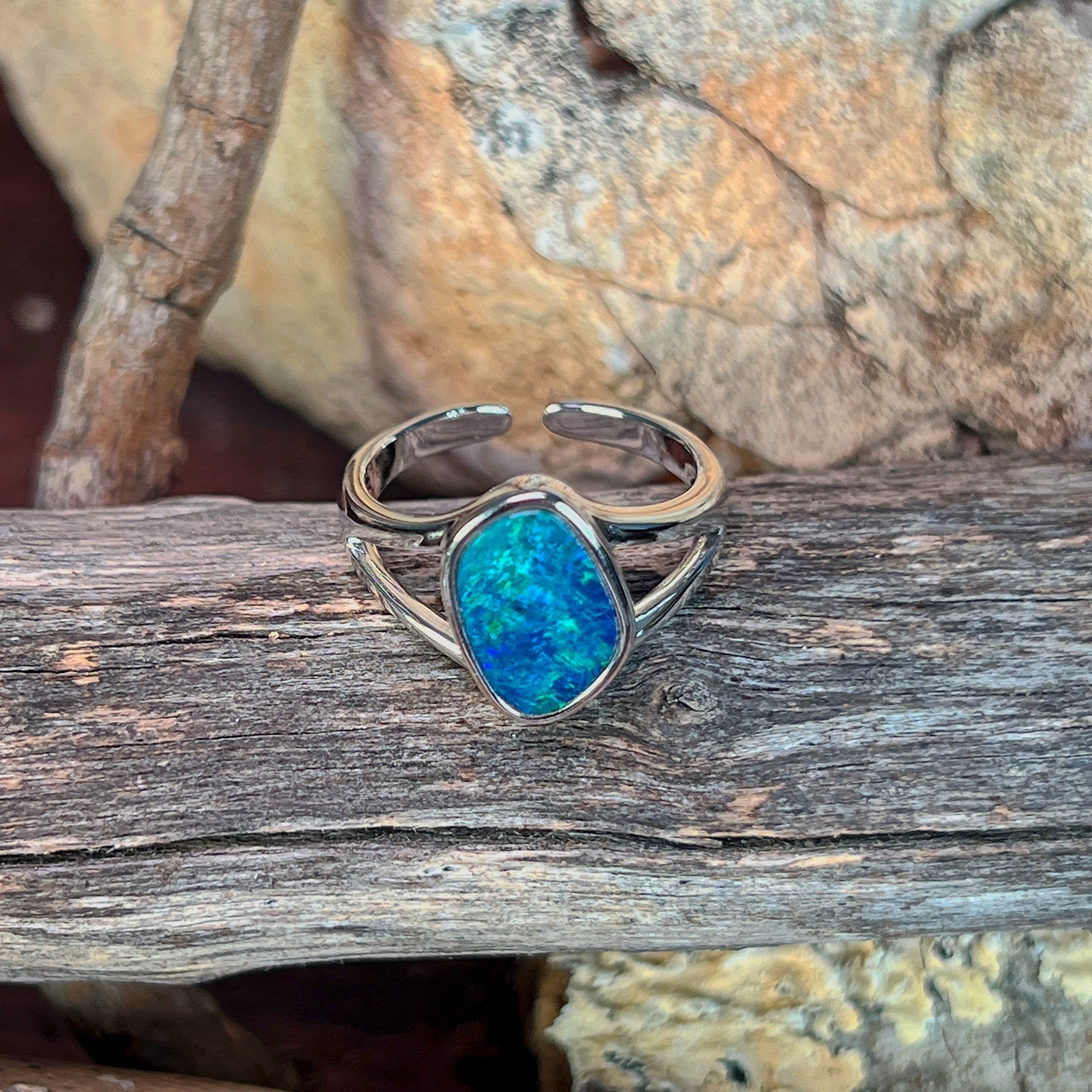 Freeform opal doublet ring in silver photographed in profile on driftwood, showing the setting