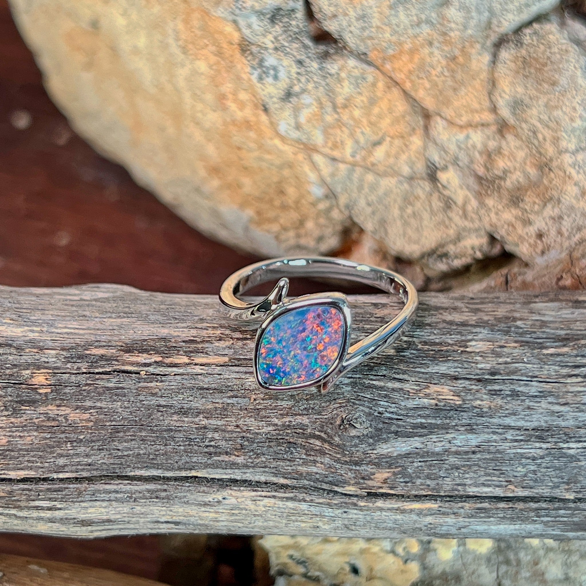 Marquise opal doublet ring in silver photographed in profile on driftwood, showing the setting