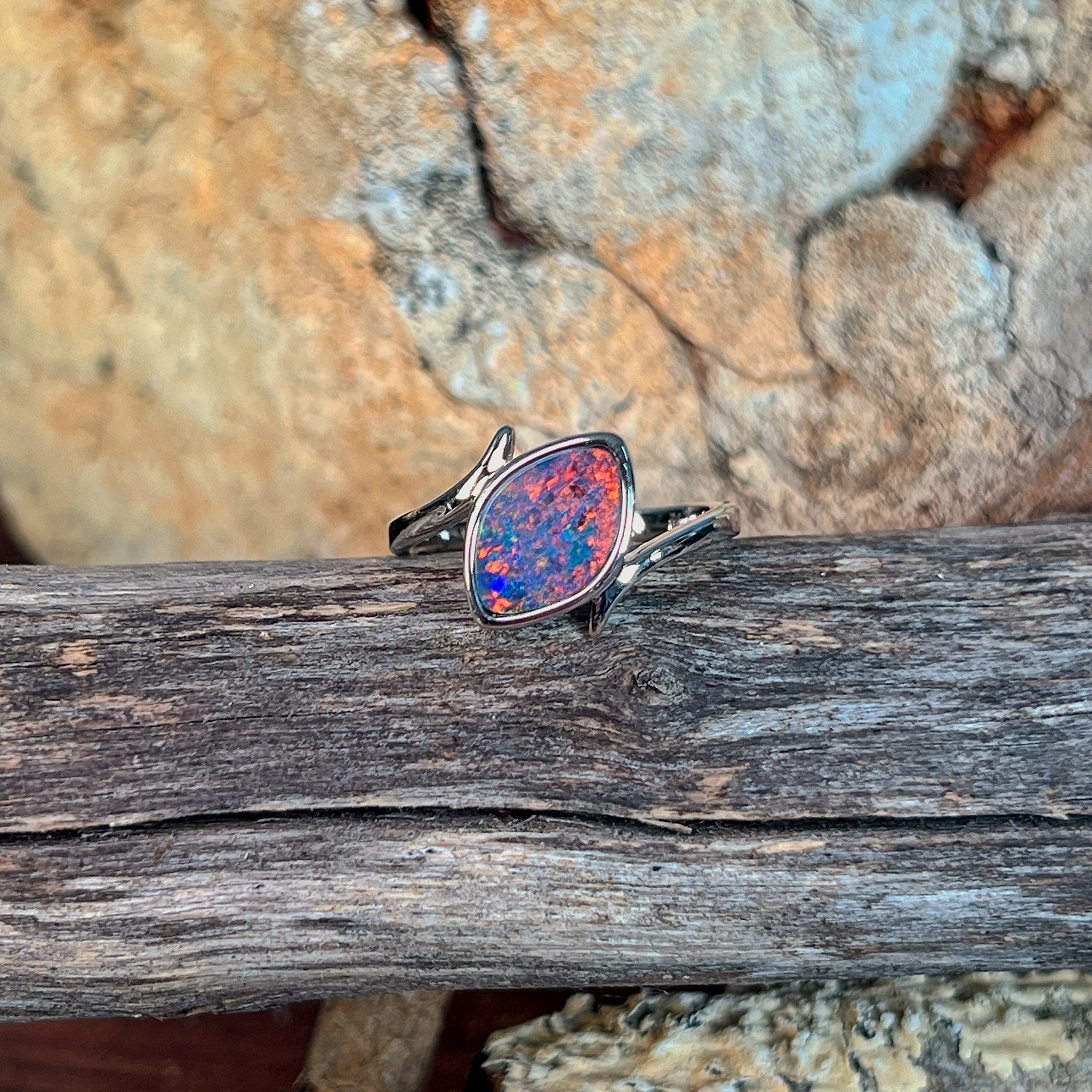 Marquise opal doublet ring in silver on driftwood, the marquise opal doublet catching the light
