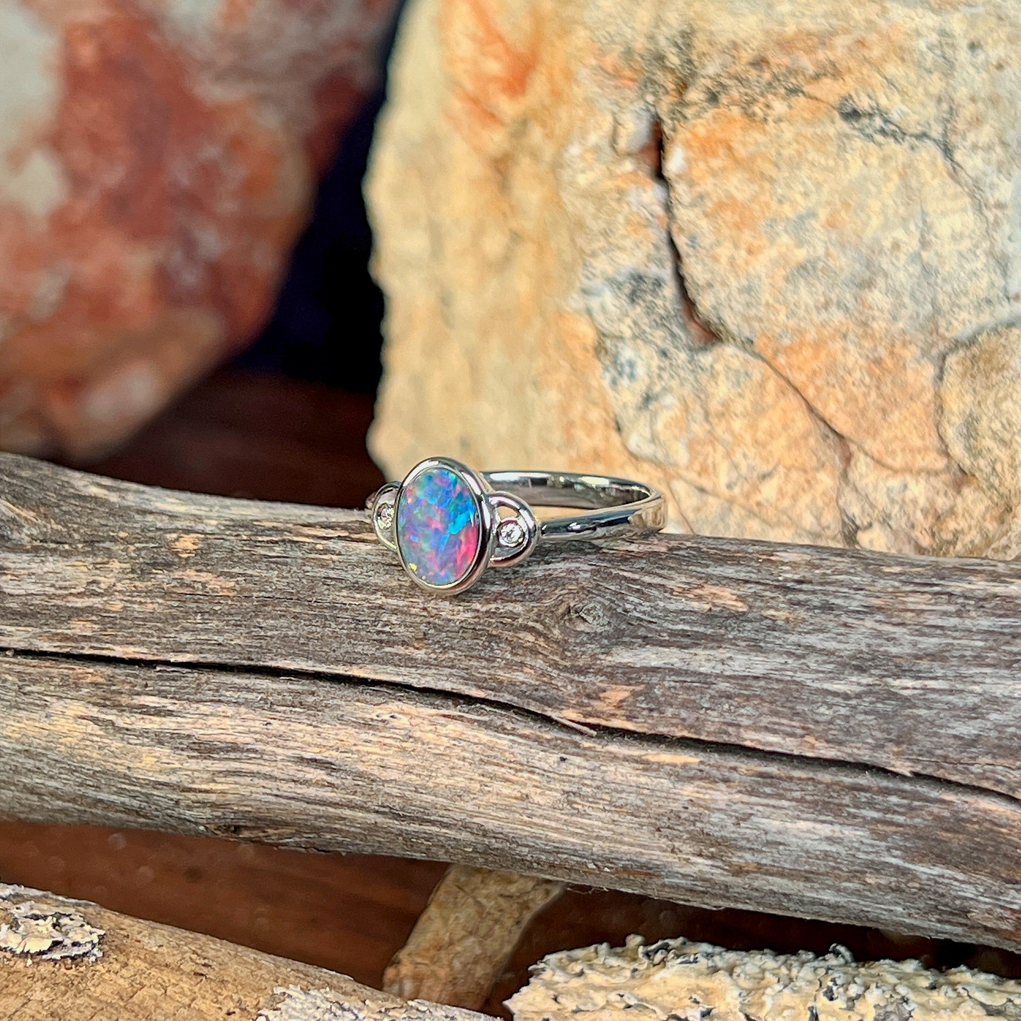 Oval opal doublet ring in silver photographed in profile on driftwood, showing the setting