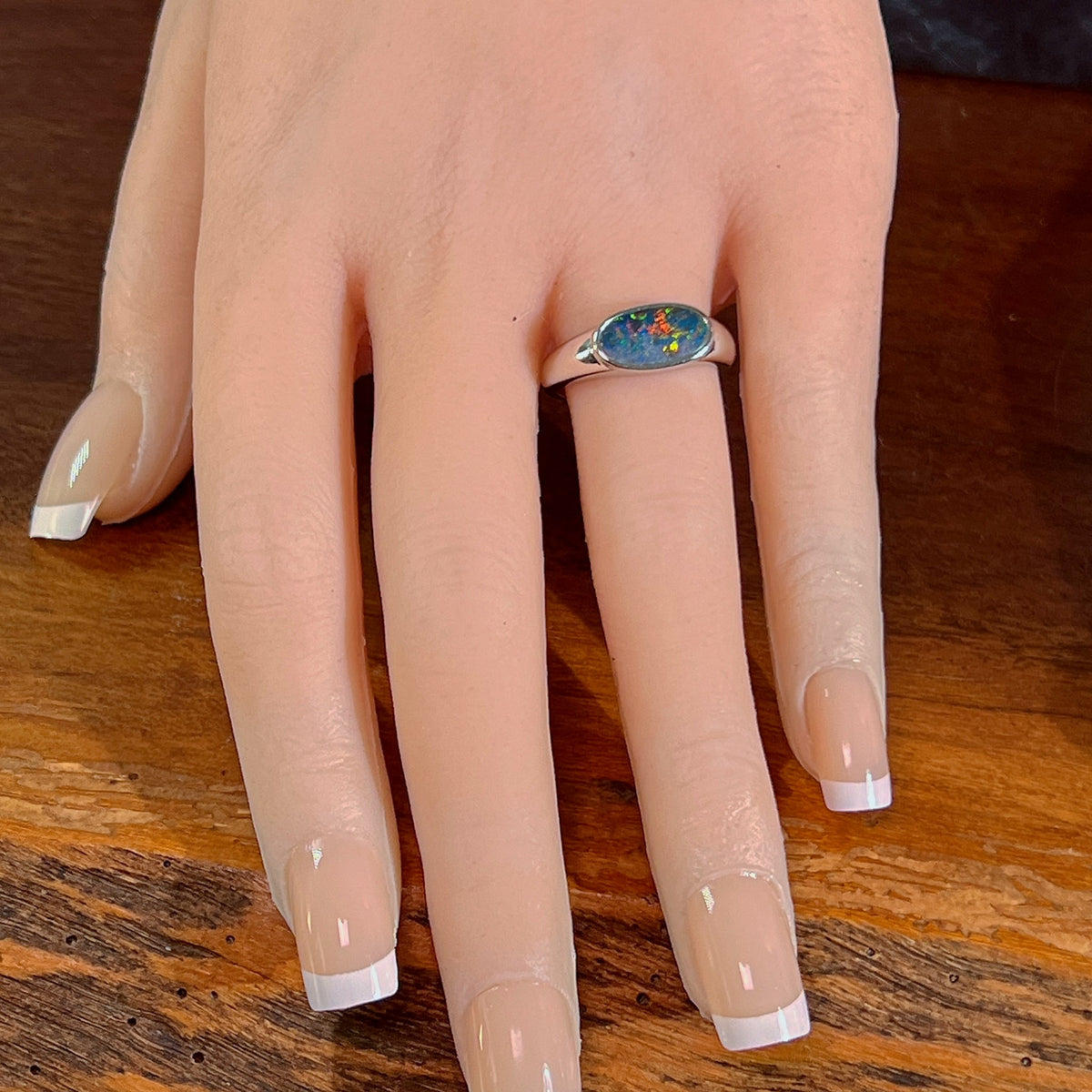 Horizontal oval opal doublet ring in silver worn on the hand, full view across the fingers