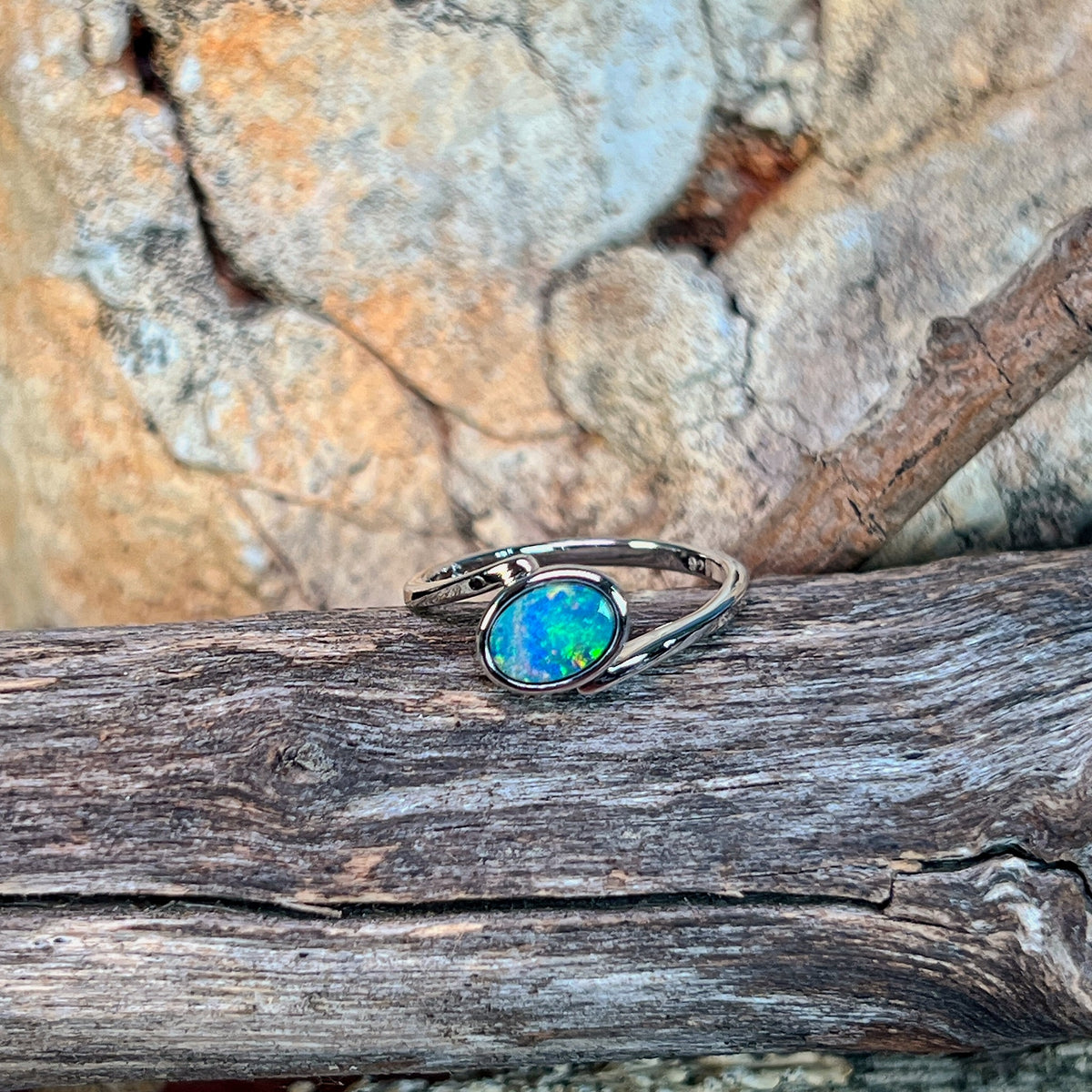 Slanted oval opal doublet ring in silver resting on weathered driftwood