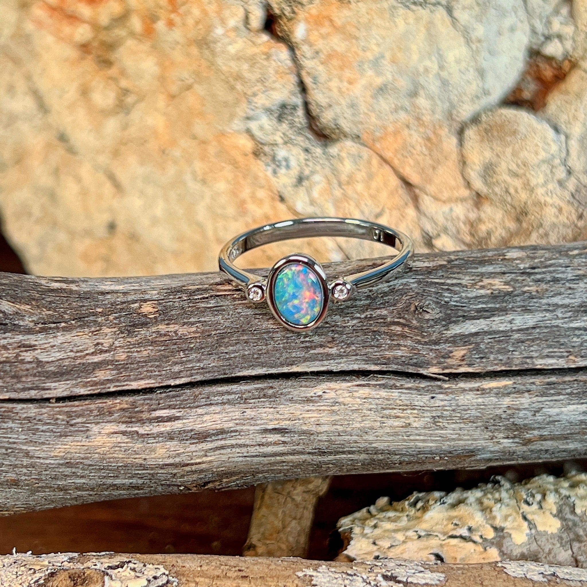 Oval opal doublet ring in silver resting on weathered driftwood
