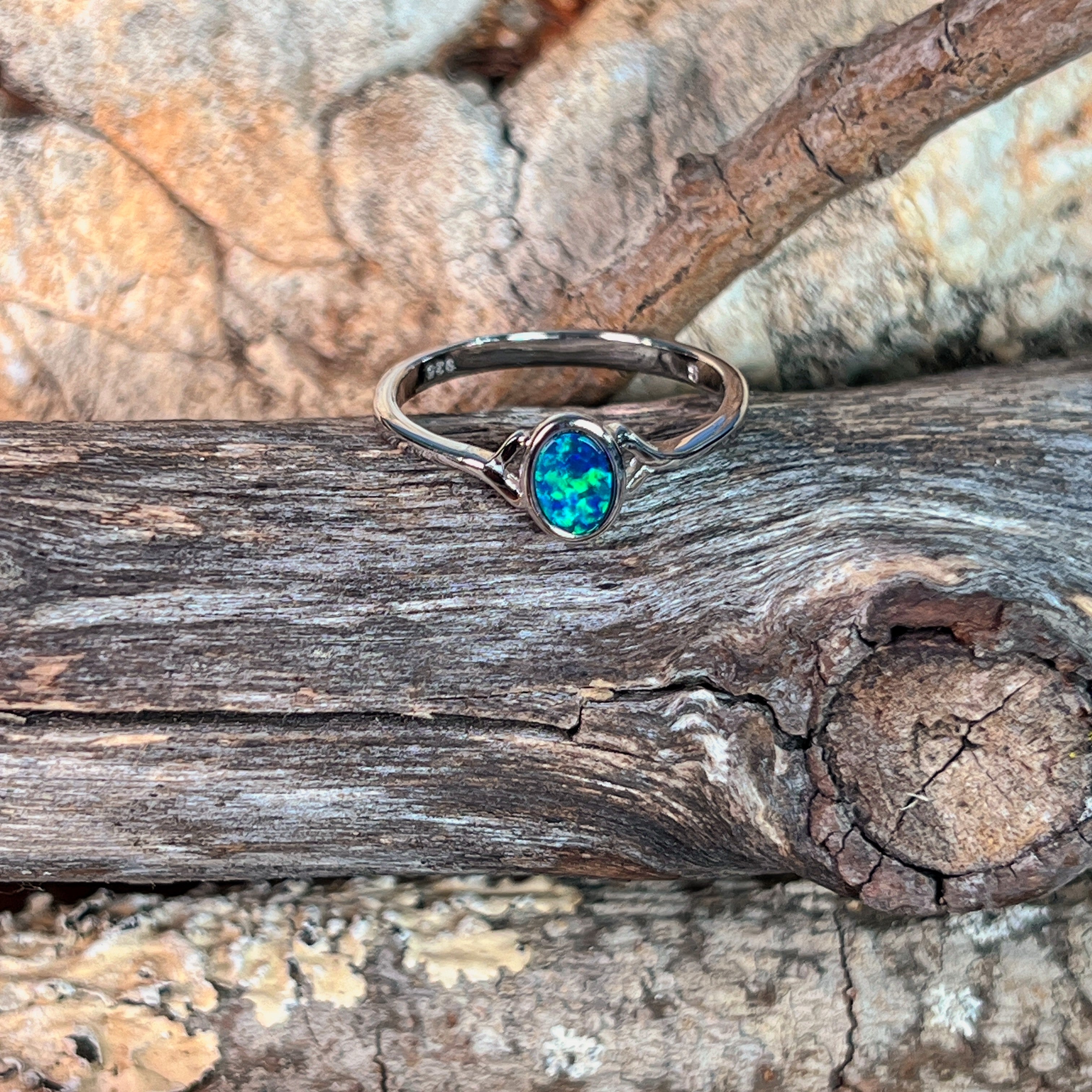 Deep green opal doublet ring in silver resting on weathered driftwood