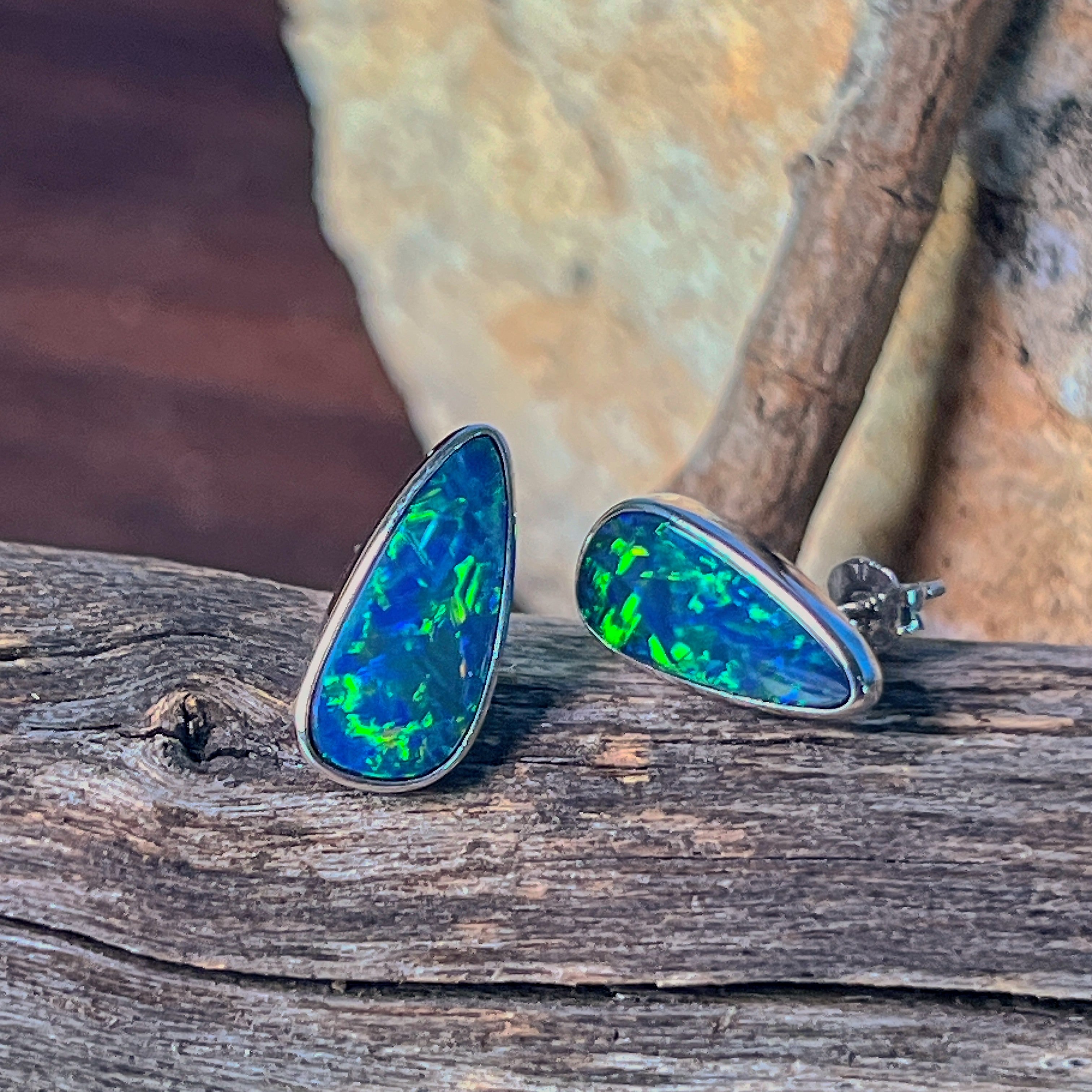 Sterling silver pear-shaped opal doublet studs standing upright on weathered driftwood