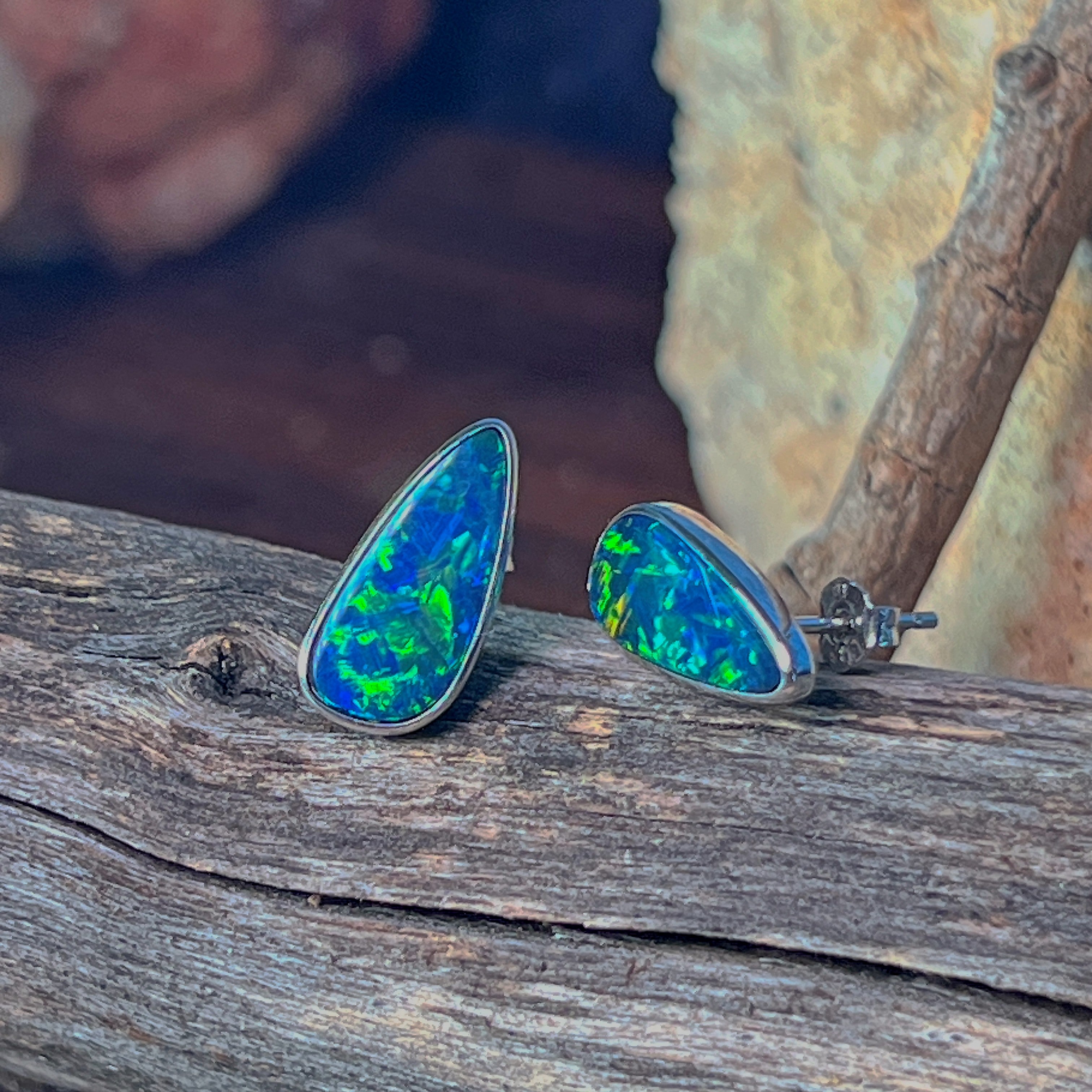 Pear-shaped opal doublet studs in sterling silver angled to catch the light on driftwood