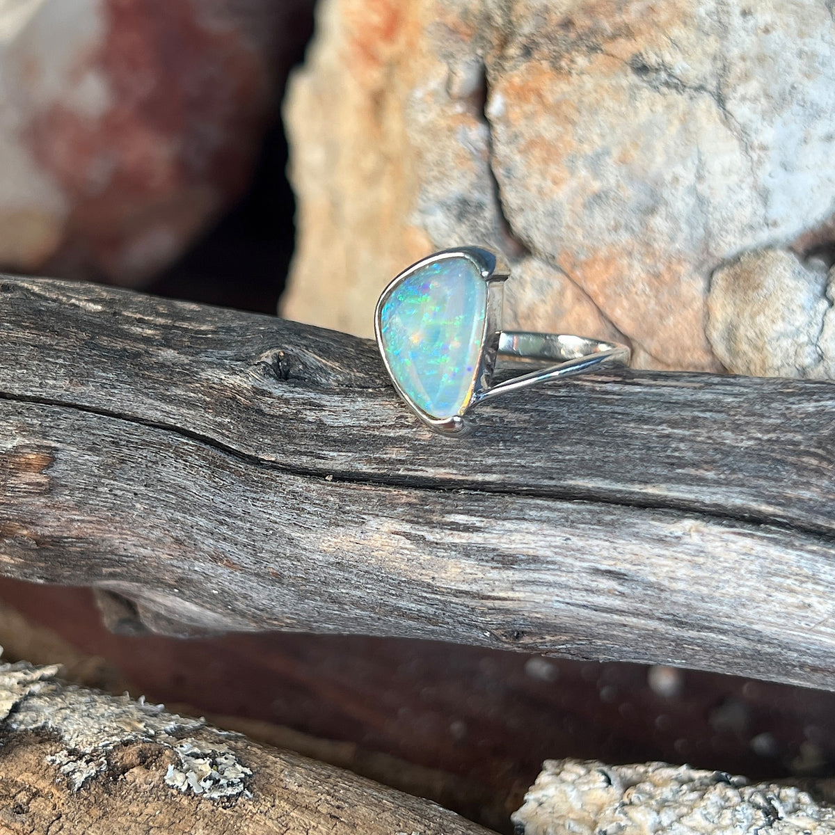 Solid crystal opal 13x10mm in a sterling silver cross over band, half bezel set, green and blue, on timber