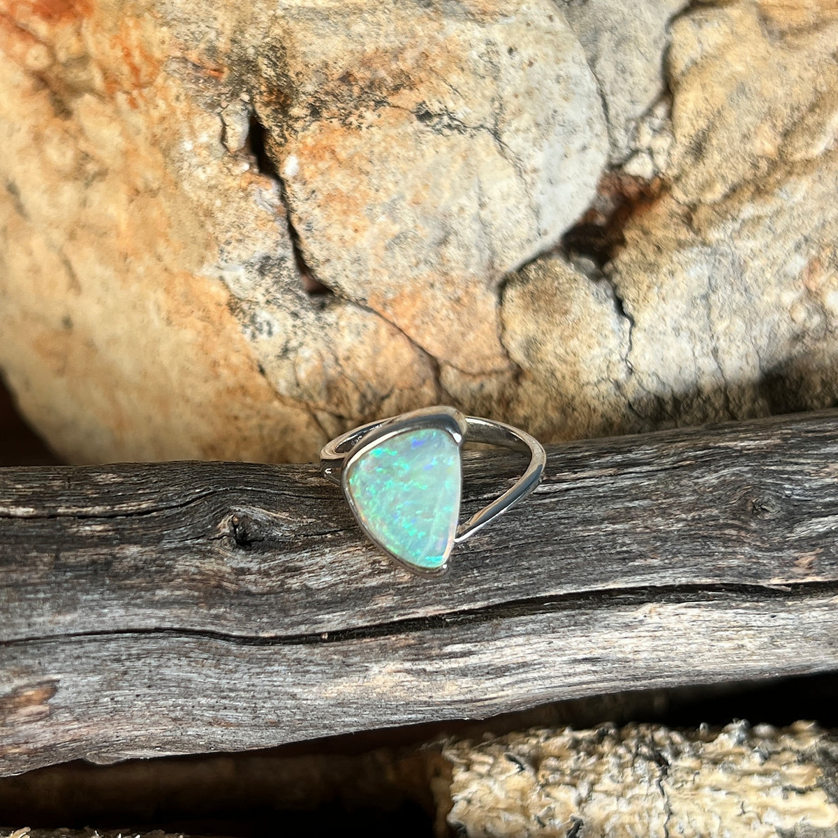 Green and blue solid crystal opal 13x10mm, triangular, sterling silver cross over ring, side view on timber