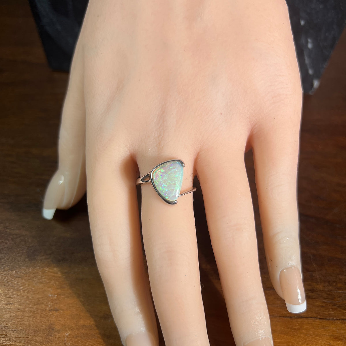 Australian crystal opal 13x10mm ring, sterling silver cross over band, solid opal, green and blue, on a display hand