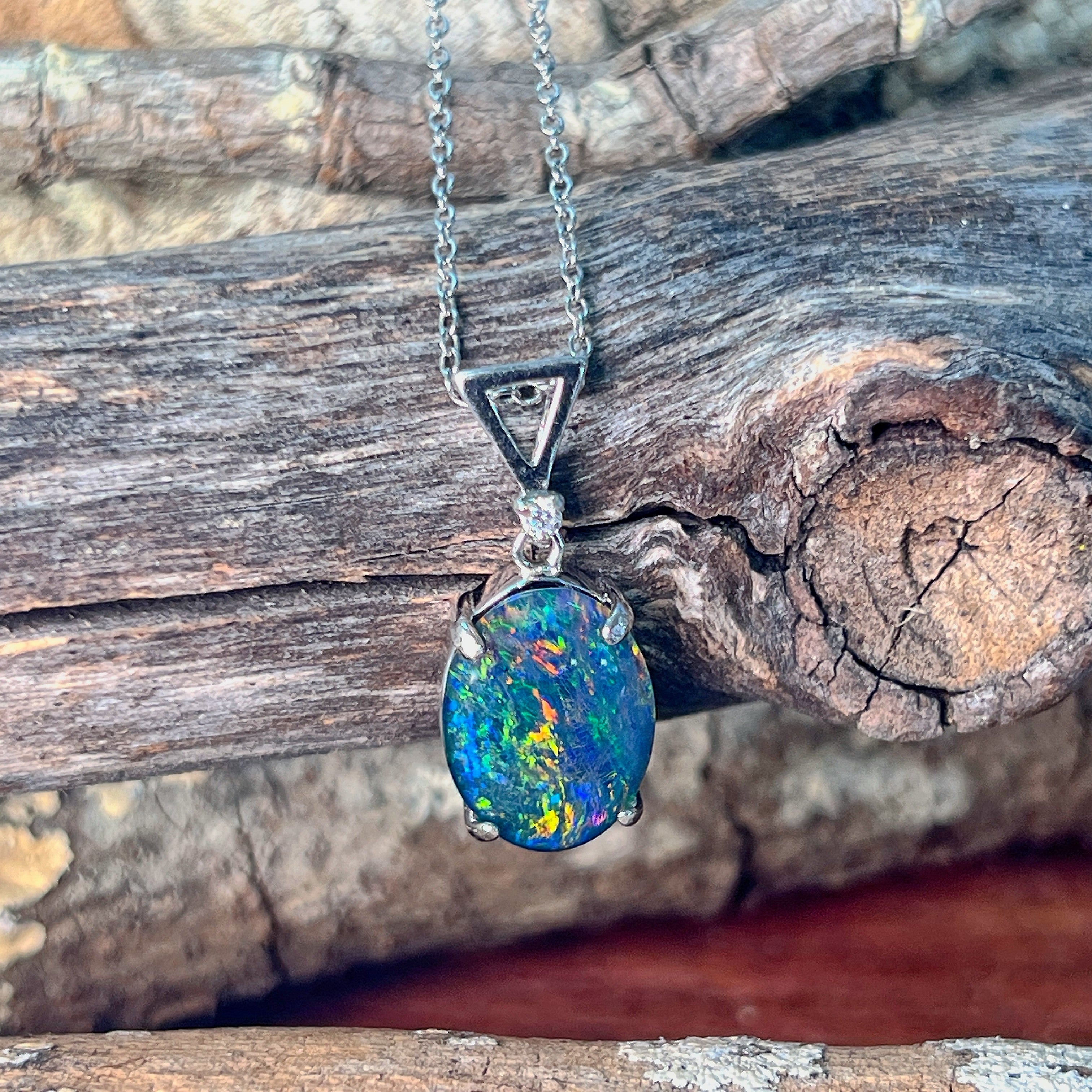 14x10mm oval opal triplet pendant in silver angled against driftwood