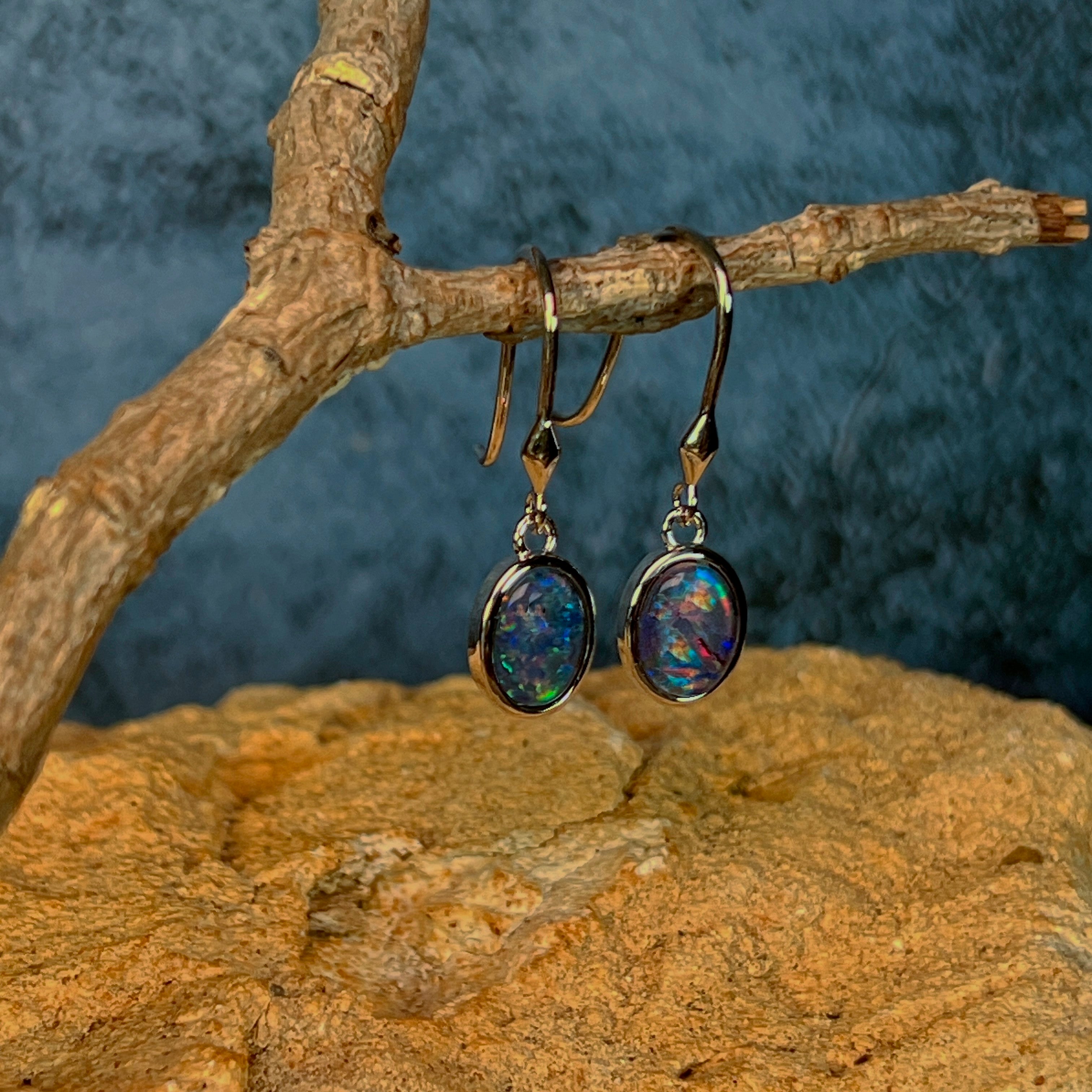 Angled view of sterling silver dangling earrings with 8x6mm oval opal triplets on a driftwood branch