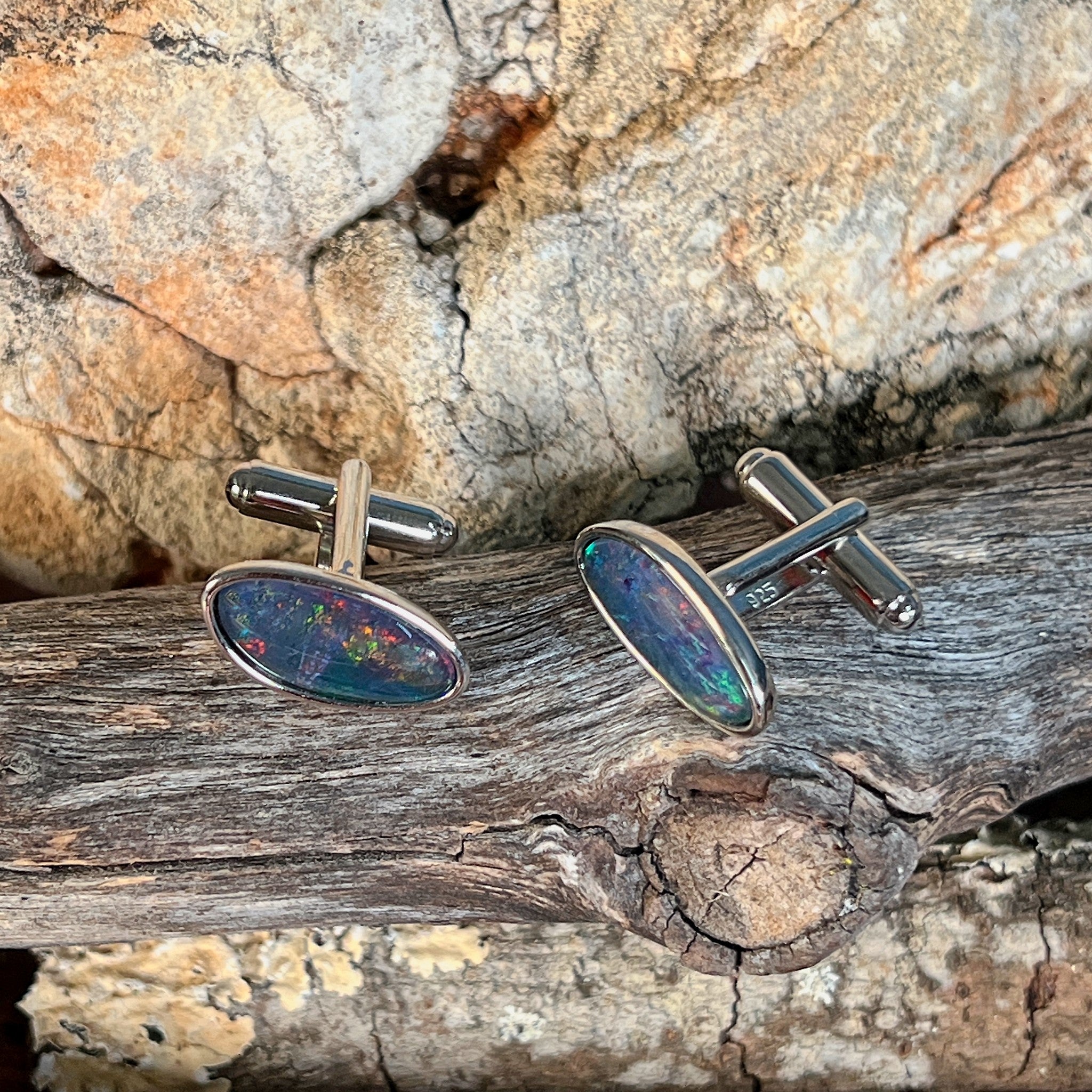 Pair of opal triplet cufflinks in silver photographed in profile on driftwood, showing the setting