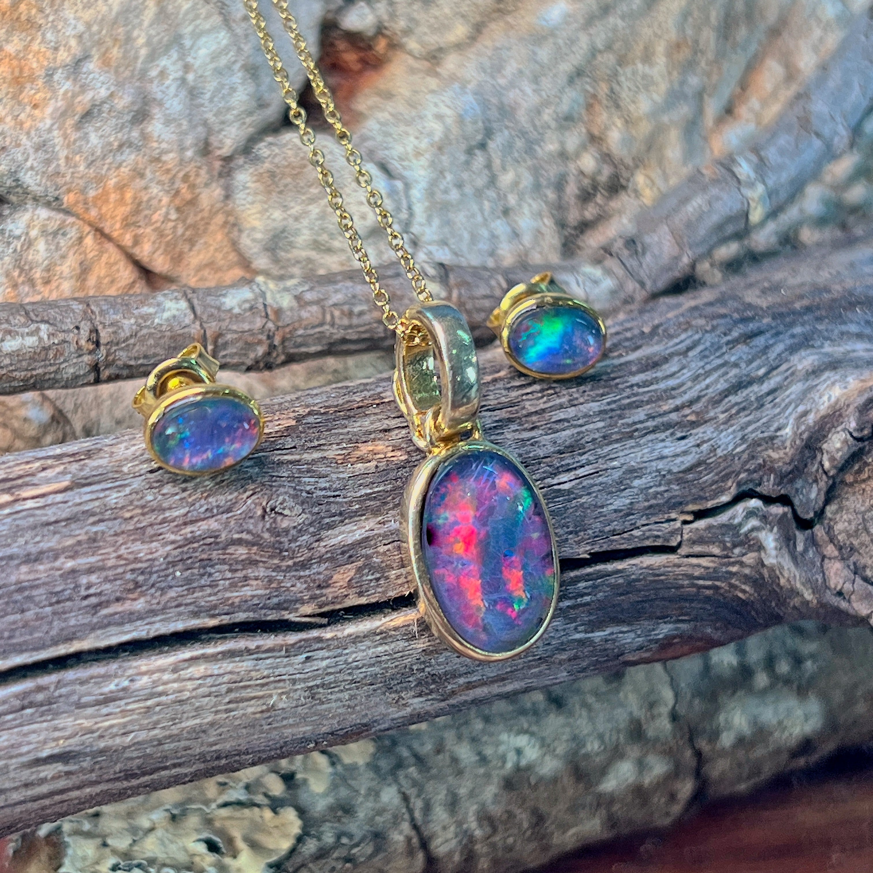 Opal triplet pendant and matching bezel-set studs in gold-plated silver against driftwood