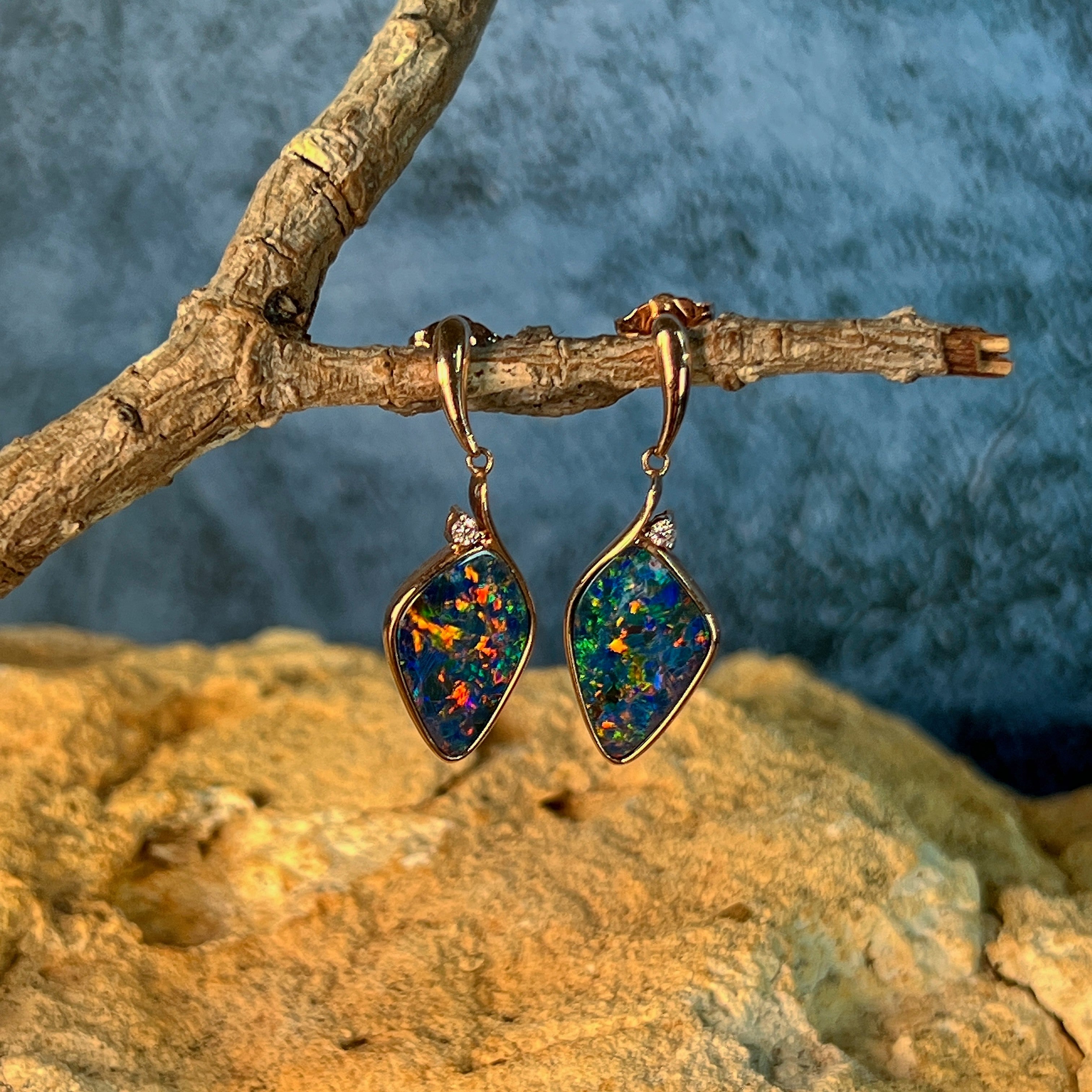 Rose gold opal doublet drop earrings hanging from a branch above sandstone