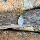 Australian white opal pendant in 18kt yellow gold, blue, red and green pinfire, shown on driftwood
