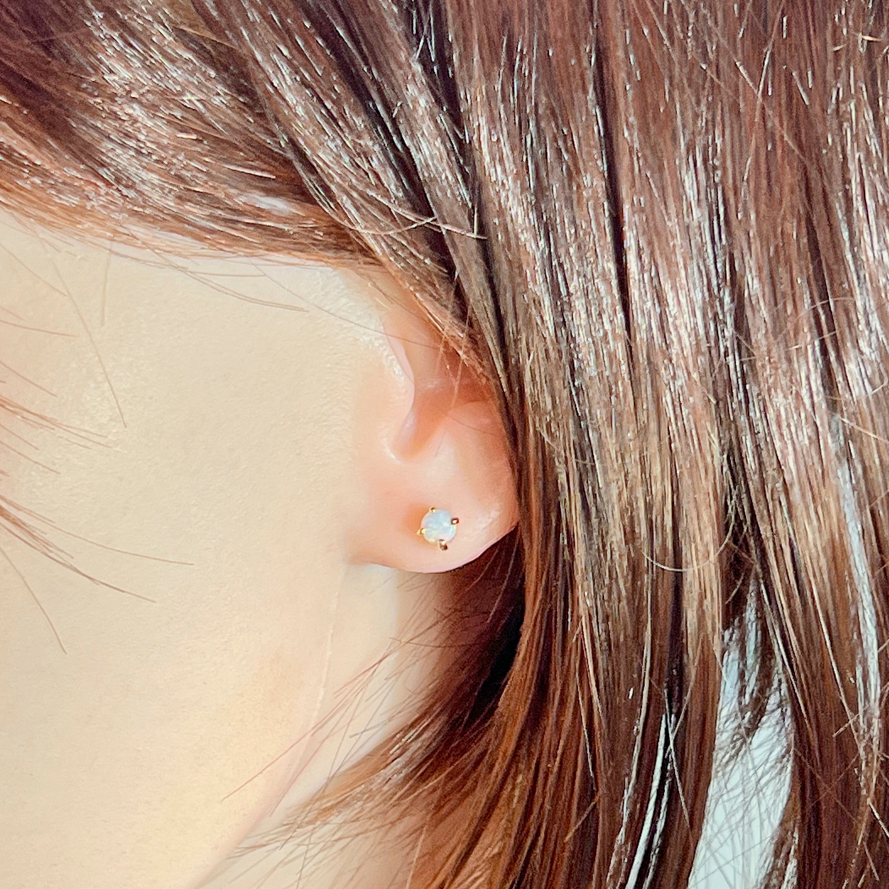 Worn view of the round crystal opal claw-set stud in 9kt yellow gold