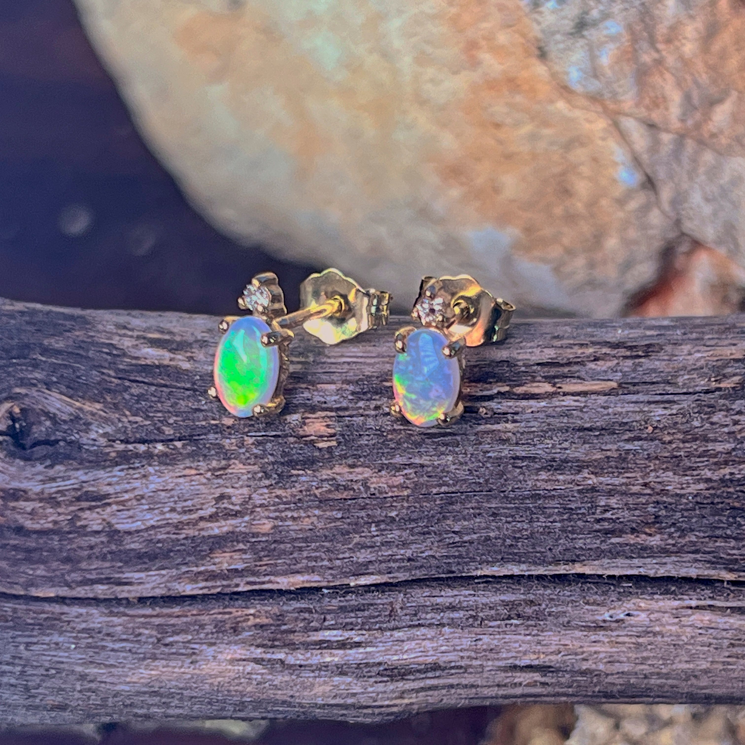 Pair of 9kt gold oval crystal opal studs with diamonds resting on driftwood