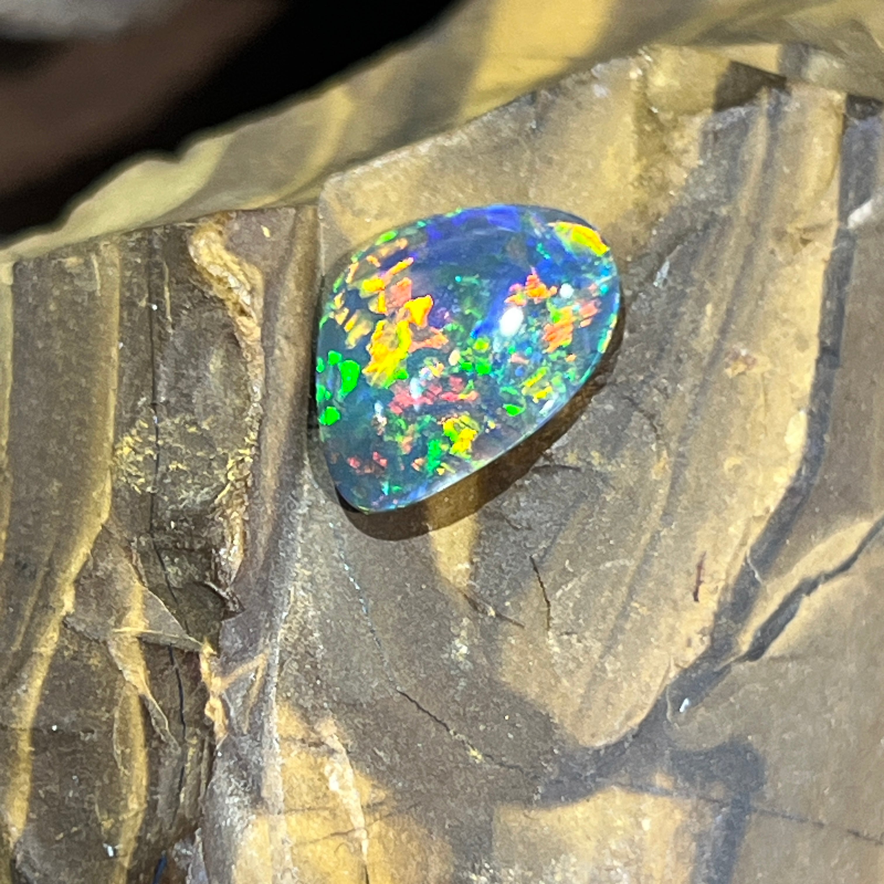1.78ct Australian black opal angled on ironstone, green and yellow fire across its teardrop outline