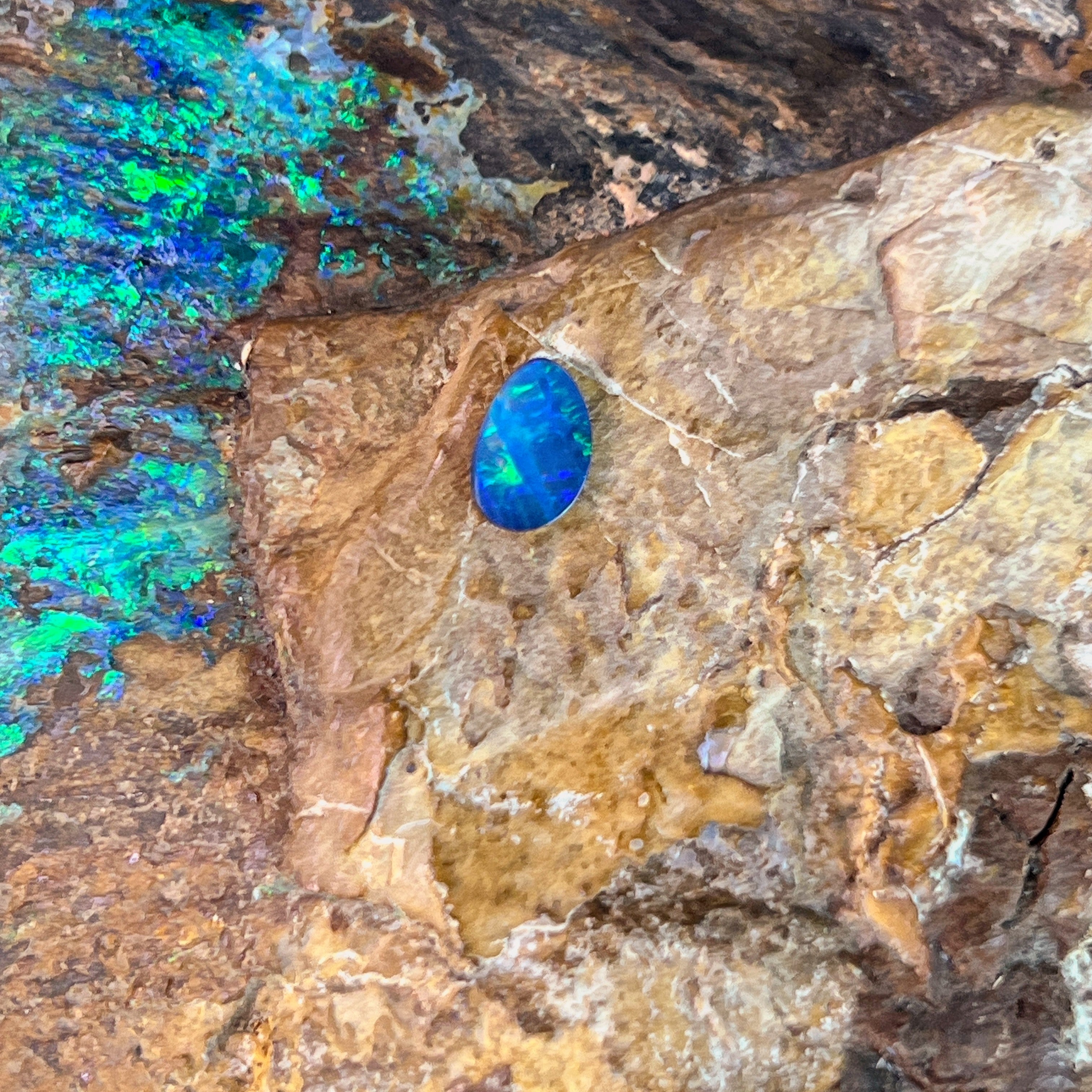 Blue violet and green fire in a freeform 0.52ct Australian opal doublet resting on rock