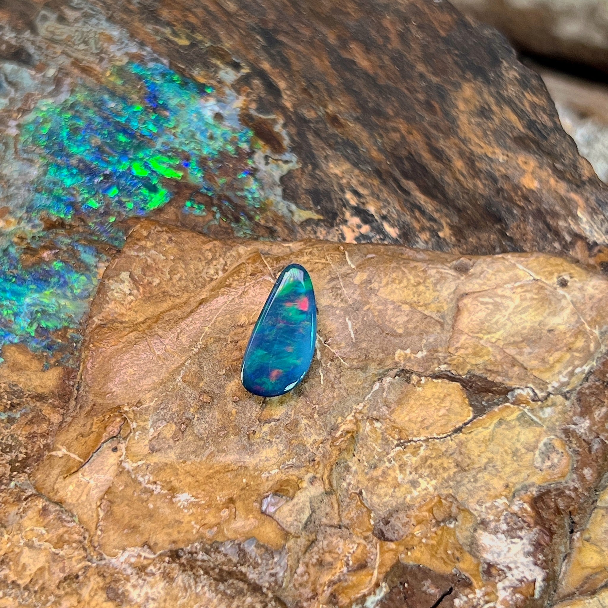 Red flashes breaking through green in a 0.74ct freeform Australian opal doublet on rock