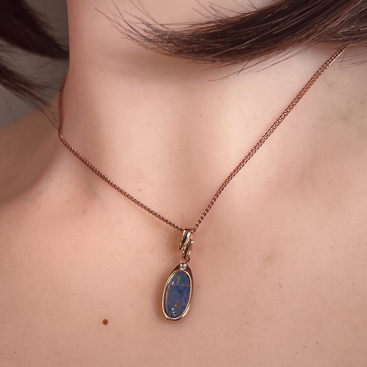 12 x 6mm oval Australian opal doublet pendant worn at the neck, rose gold-plated silver