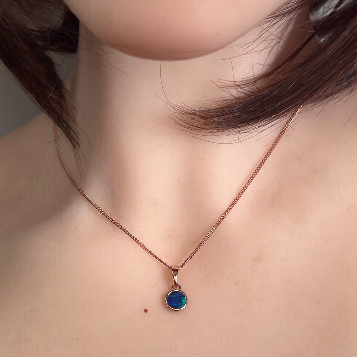 Australian opal doublet pendant worn, 6mm round stone in rose gold-plated silver