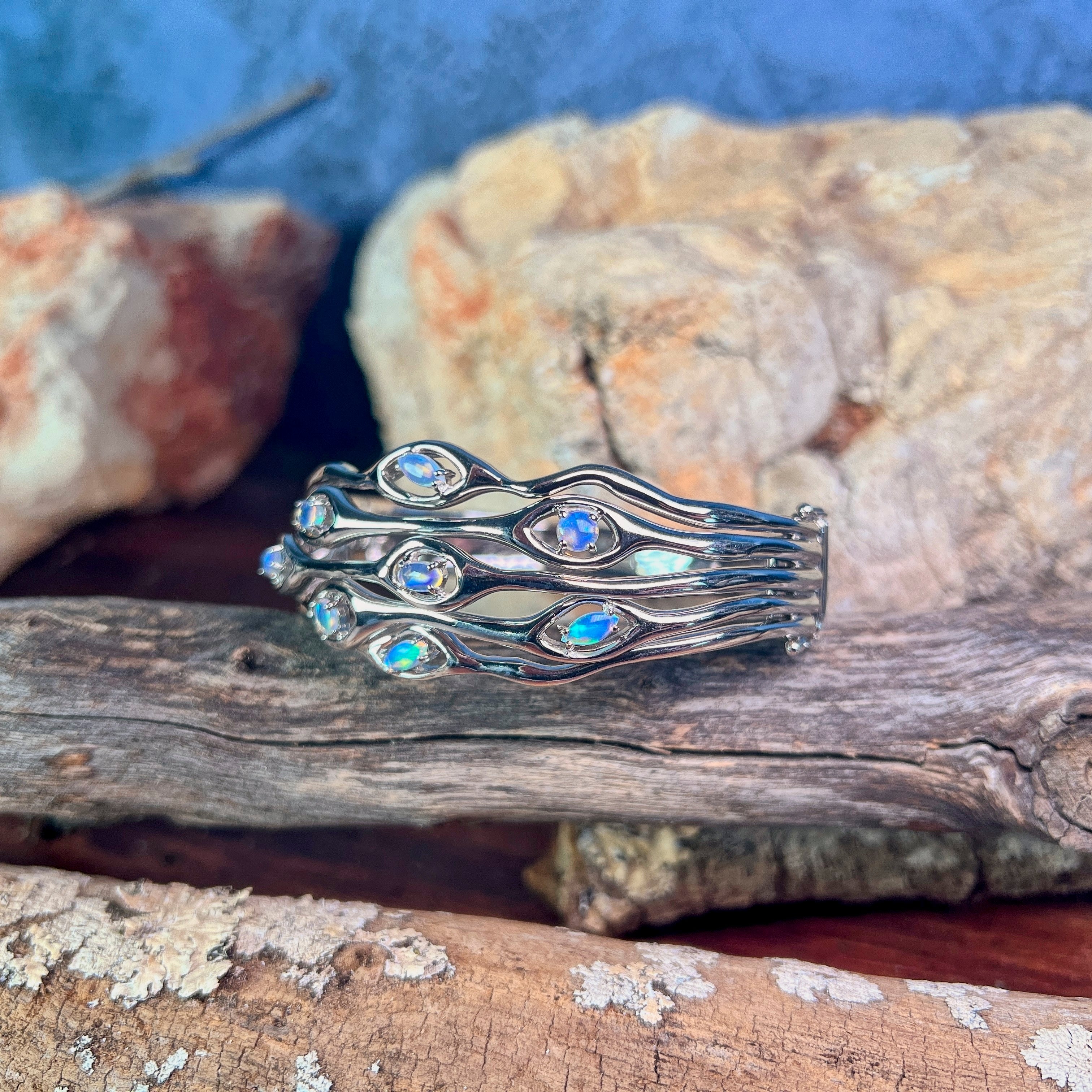 Sterling silver opal wave bangle on driftwood, showing blue and green play-of-colour