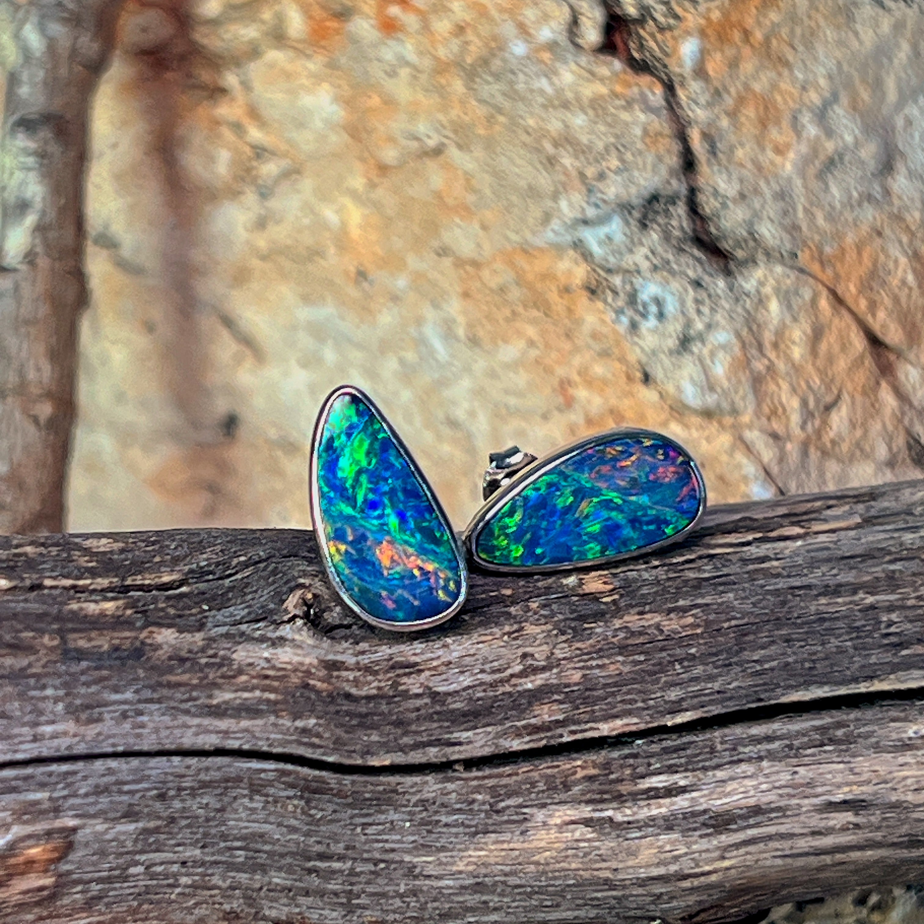 Freeform opal doublet studs in sterling silver against driftwood and sandstone