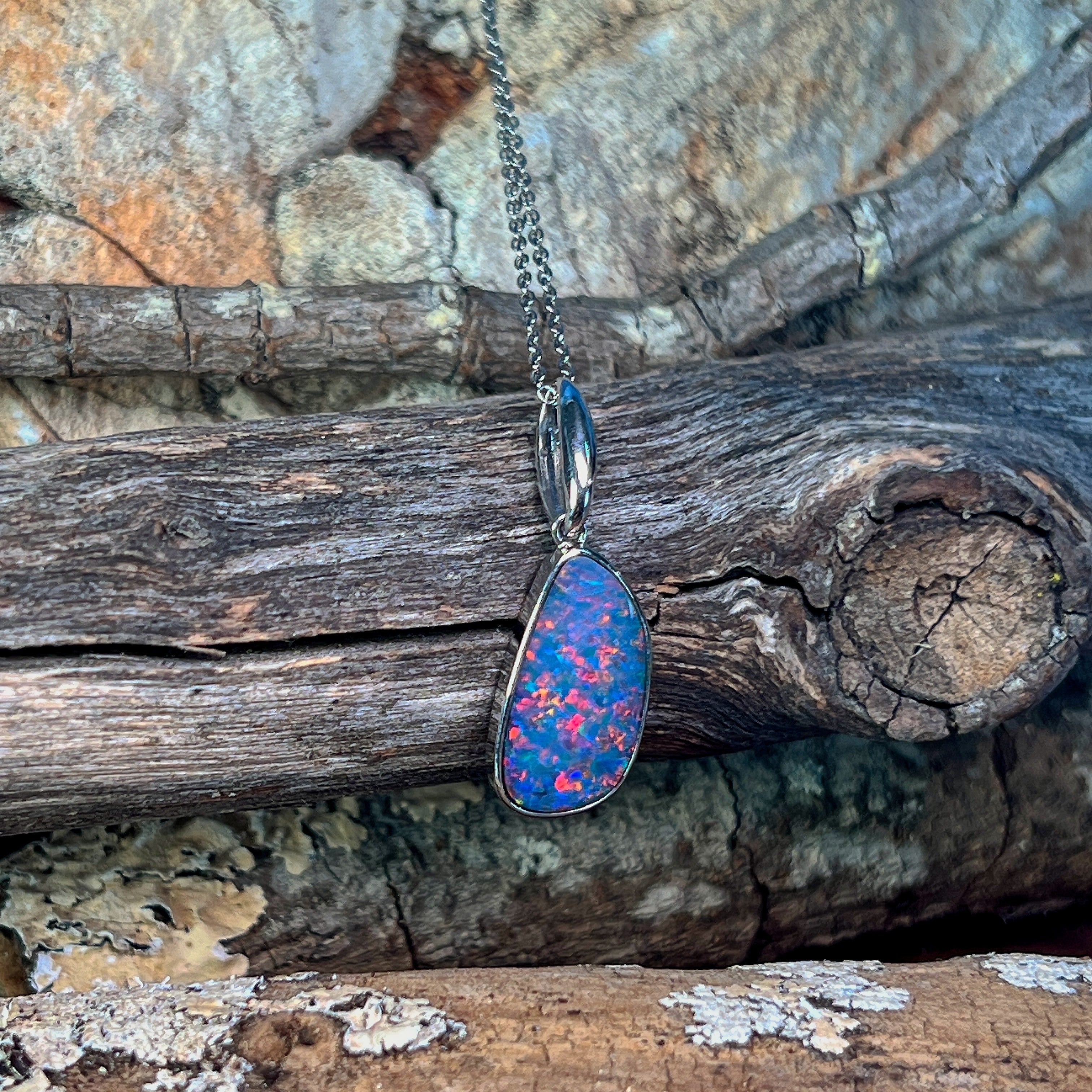 Freeform opal doublet pendant in silver showing pink and red fire across the stone