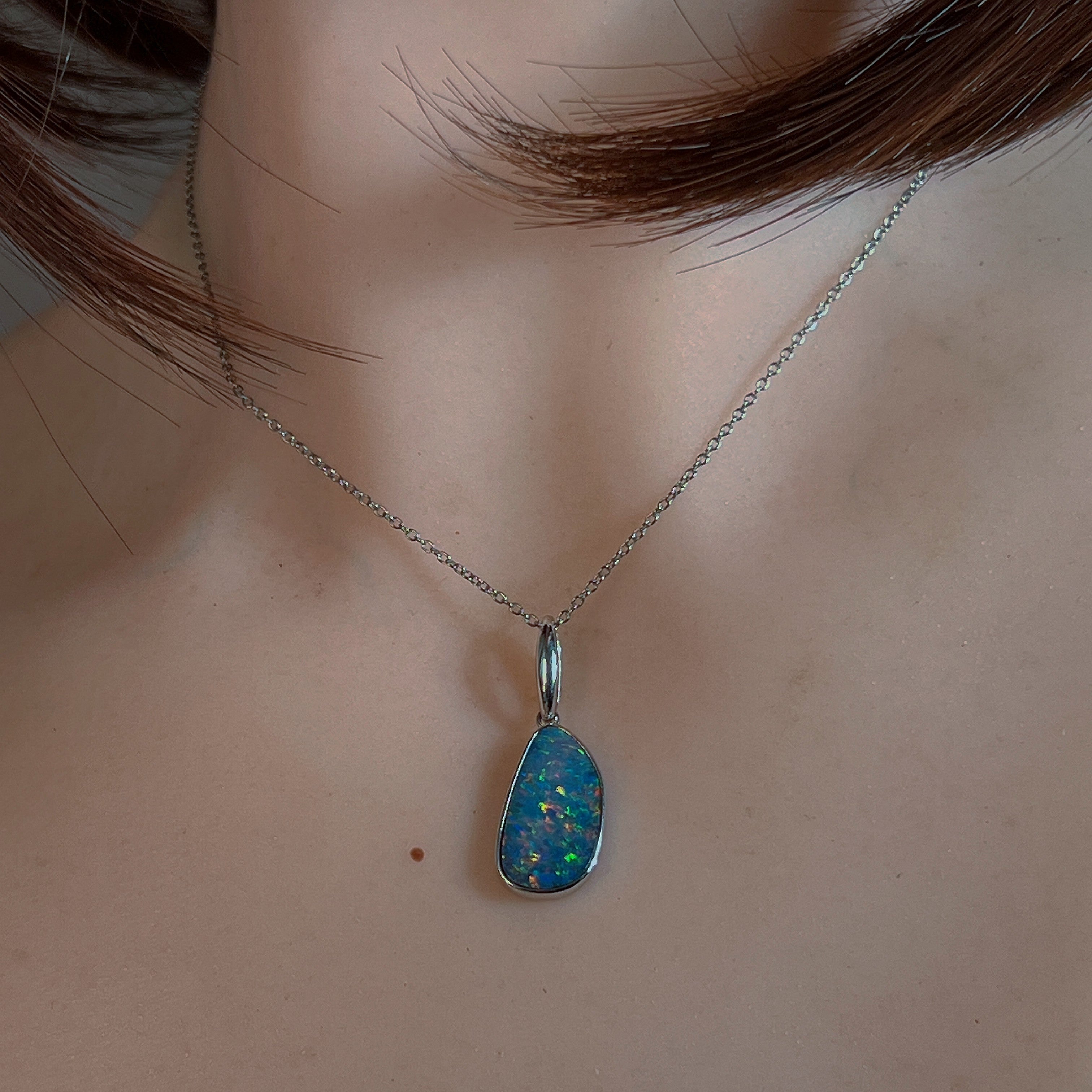 Blue-red opal doublet pendant worn at the neck, showing its scale on the collarbone