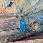 Freeform opal doublet pendant necklace in sterling silver against driftwood and sandstone