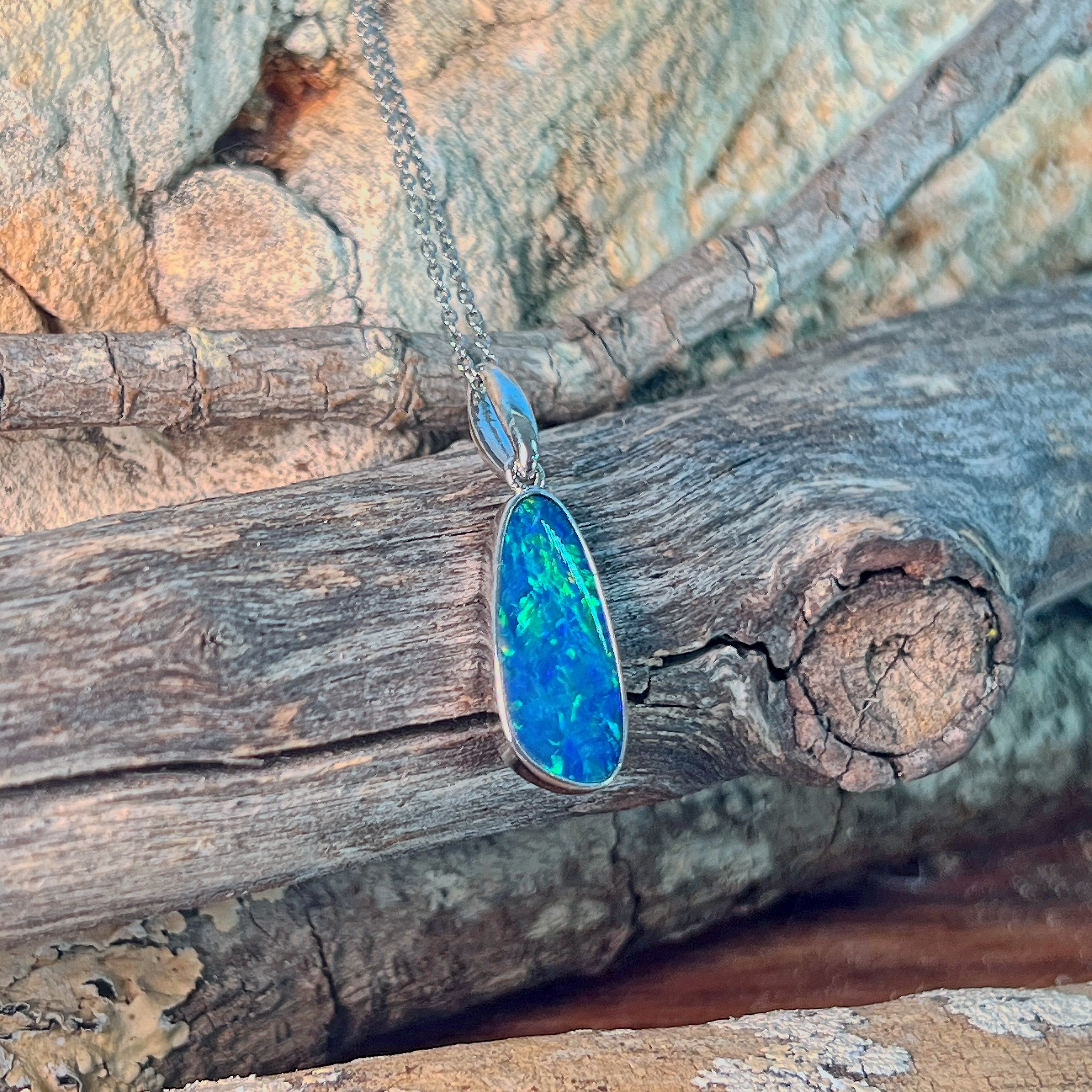 Freeform opal doublet pendant necklace in sterling silver against driftwood and sandstone
