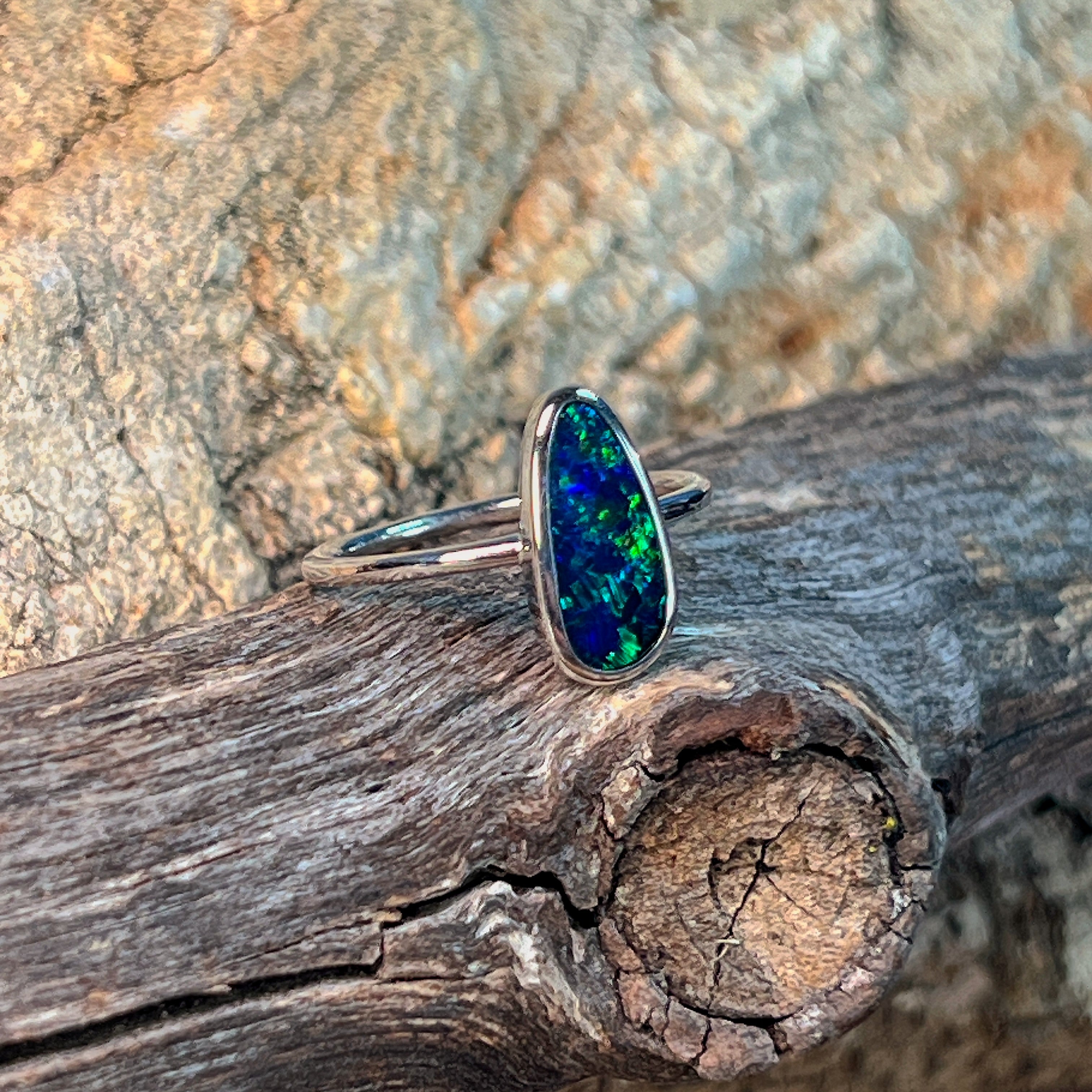 Bezel-set freeform opal doublet in silver, close view against driftwood and sandstone