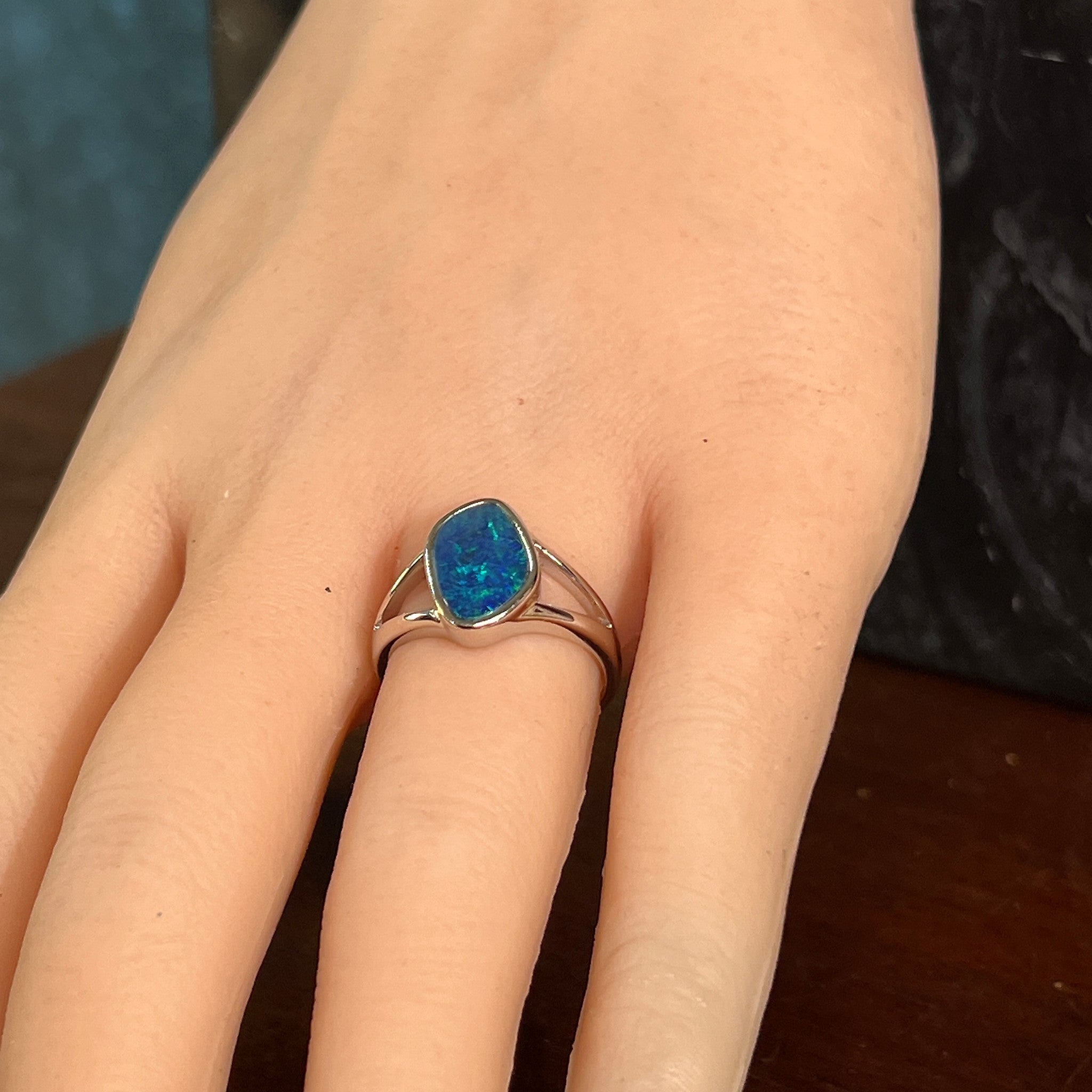 Freeform opal doublet ring in silver on the hand, angled to catch the blue and green play of colour