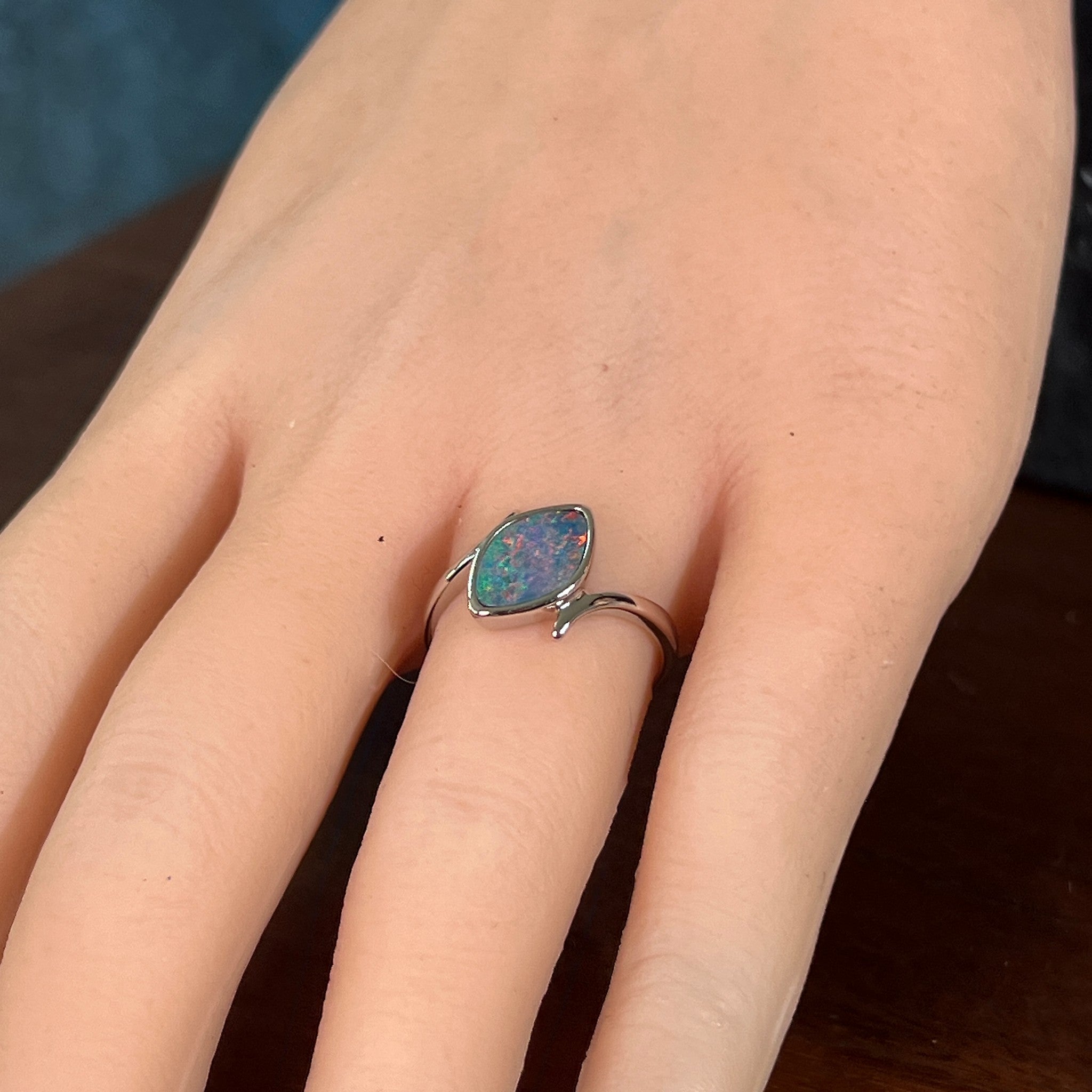 Marquise opal doublet ring in silver on the hand, angled to catch the blue, red and green play of colour