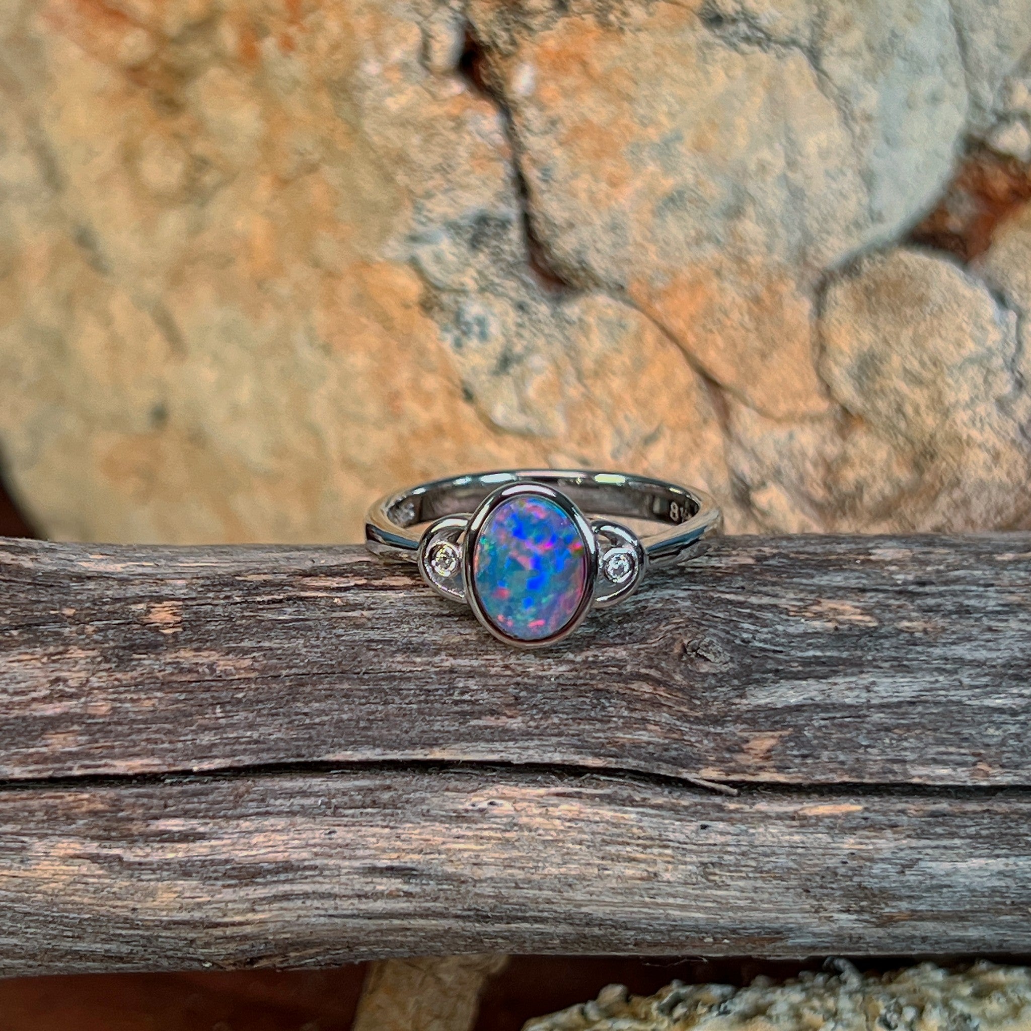 Oval opal doublet ring in silver resting on weathered driftwood