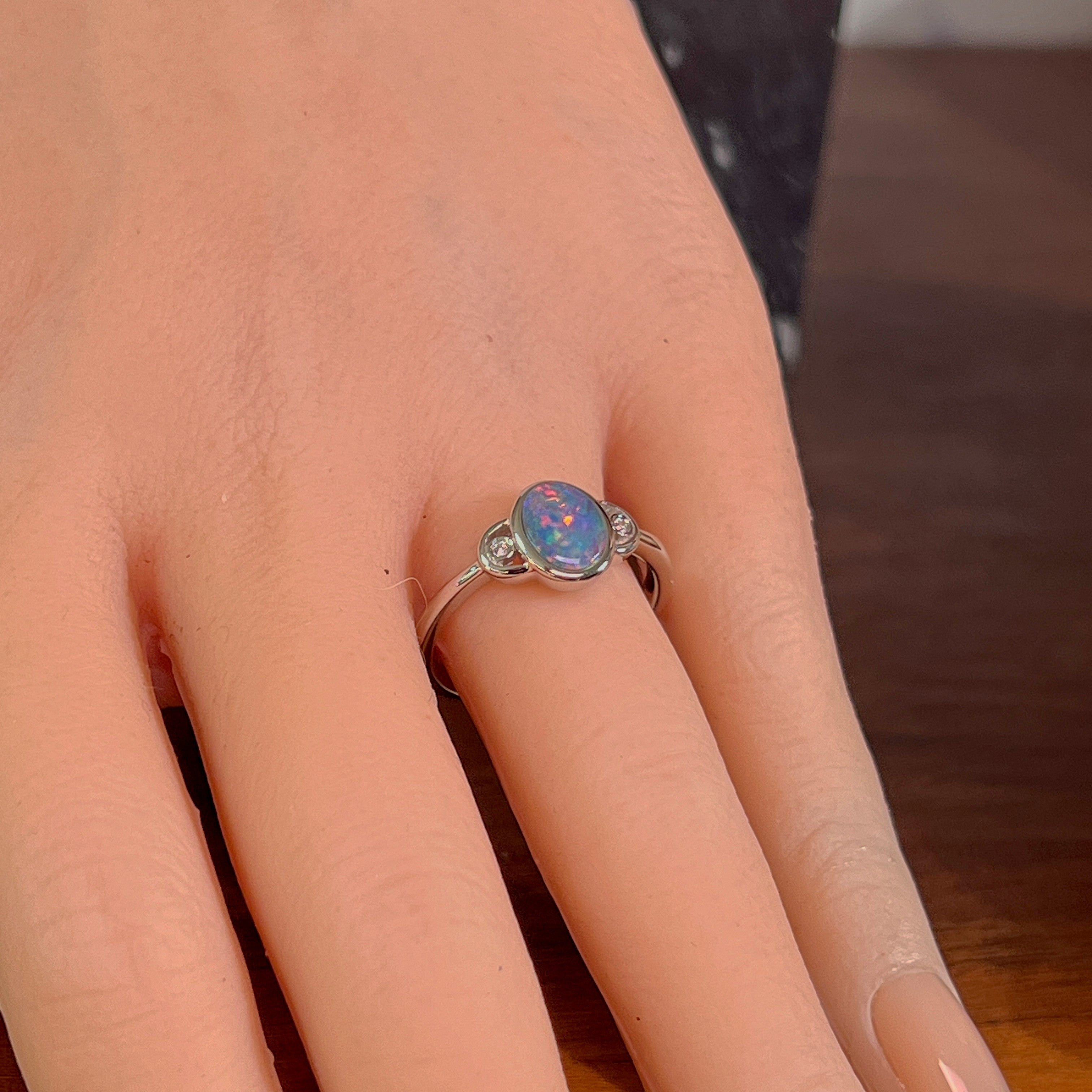 Oval opal doublet ring in silver worn on the hand, viewed across the fingers