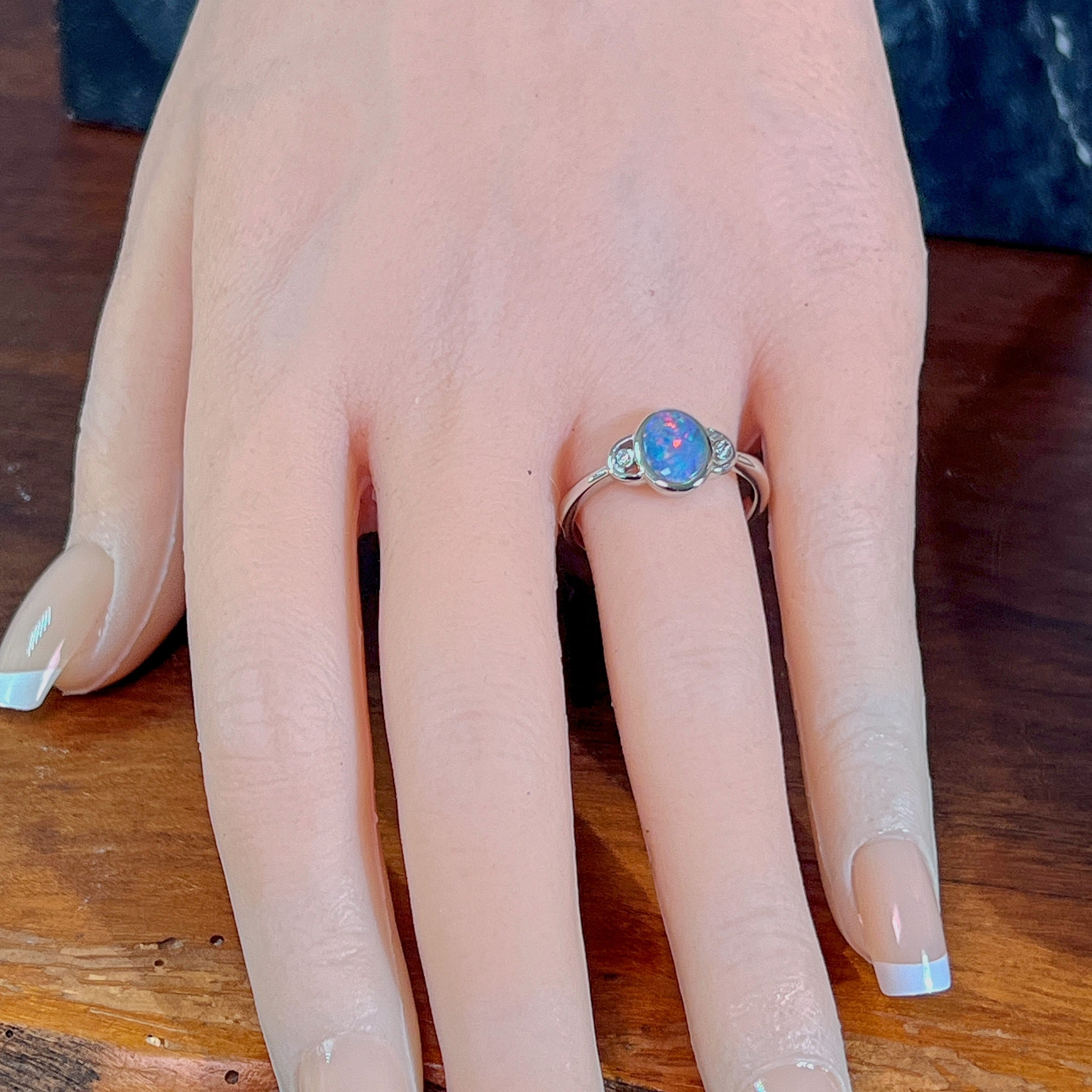 Oval opal doublet ring in silver on the hand, angled to catch the blue, red and green play of colour
