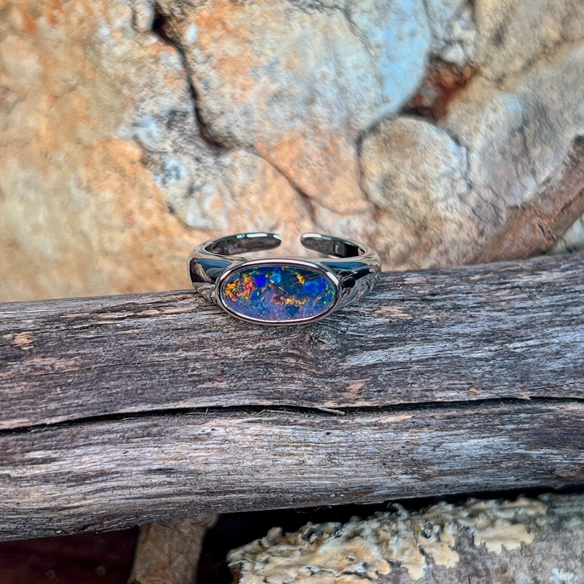 Horizontal oval opal doublet ring in silver resting on weathered driftwood