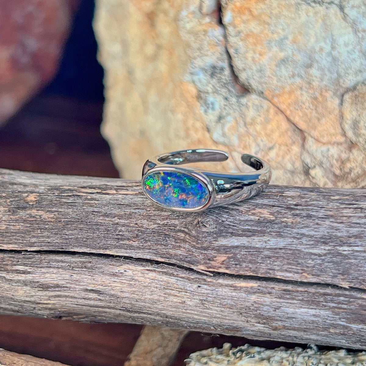 Horizontal oval opal doublet ring in silver on driftwood against Australian sandstone