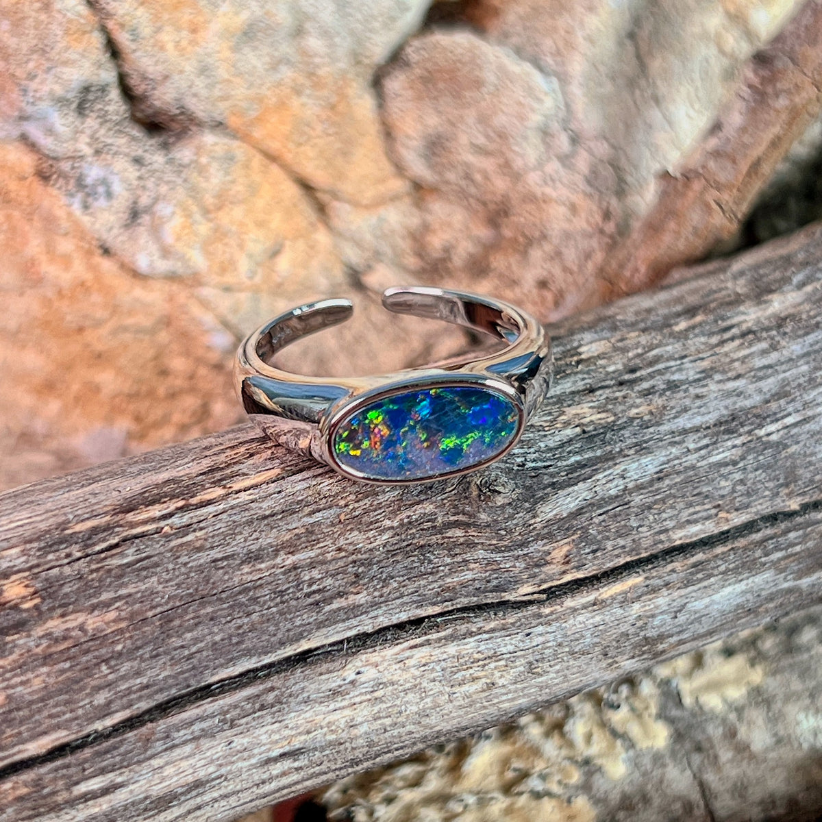 Horizontal oval opal doublet ring in silver photographed in profile on driftwood, showing the setting