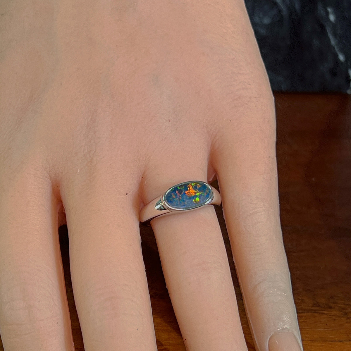 Horizontal oval opal doublet ring in silver worn on the hand, viewed across the fingers