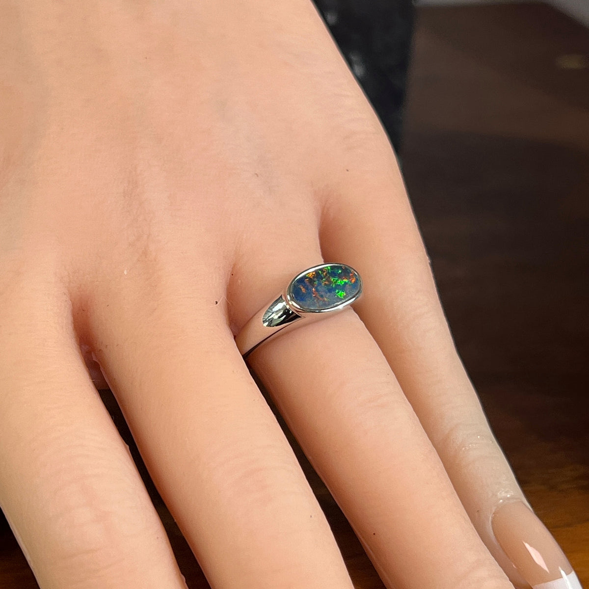 Horizontal oval opal doublet ring in silver worn on the hand, showing its scale on the finger