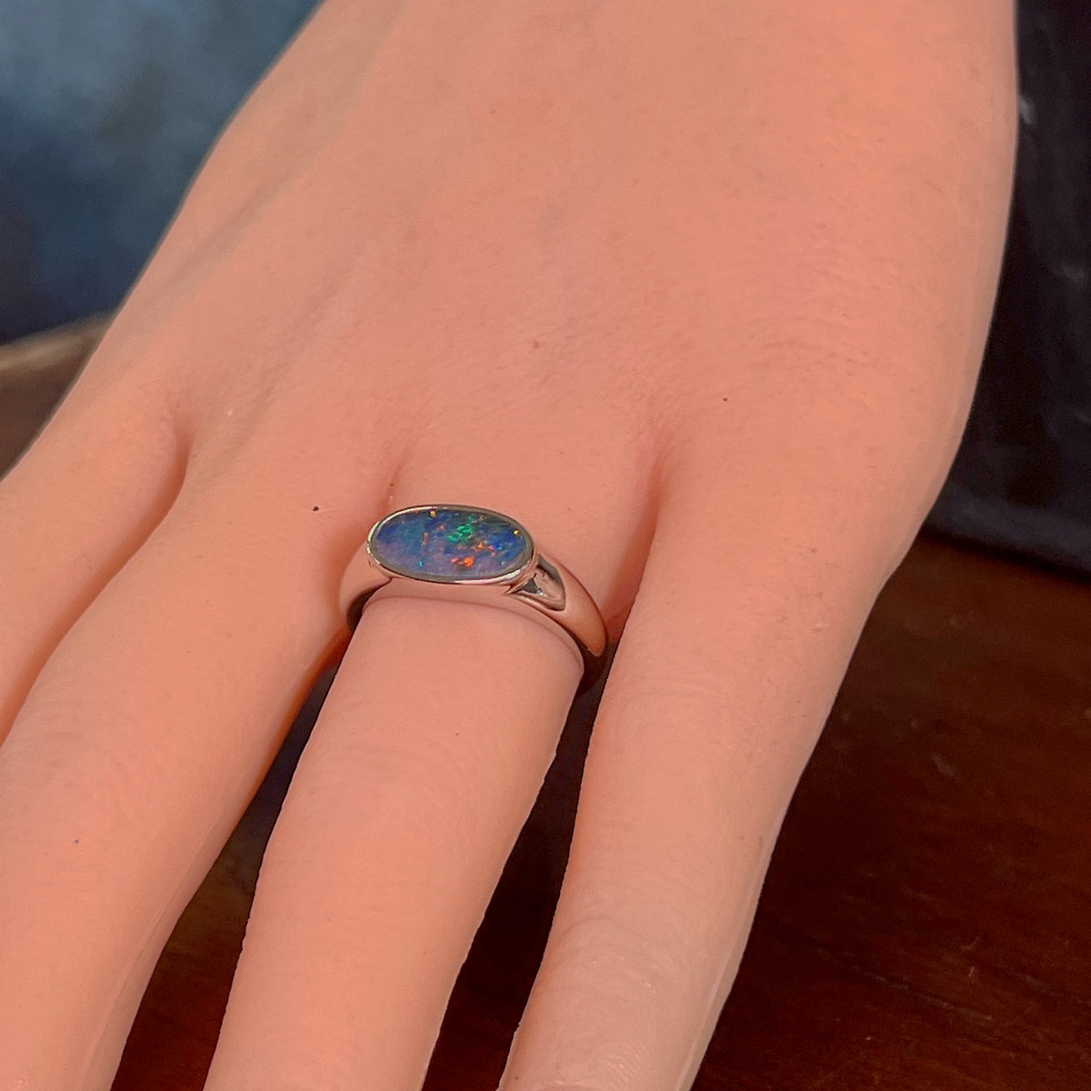 Horizontal oval opal doublet ring in silver on the hand, angled to catch the yellow, red and green play of colour